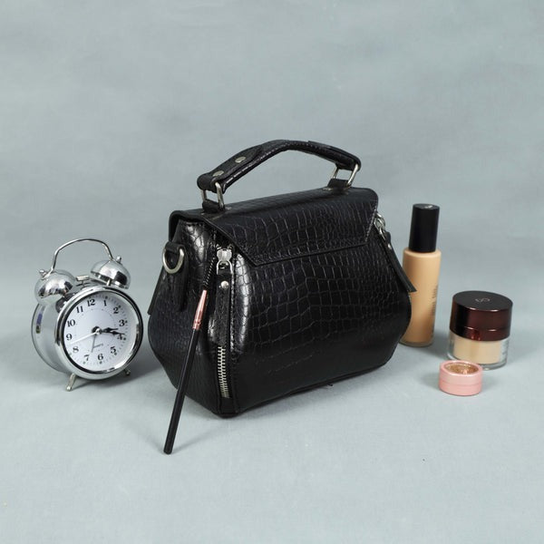 Black handbag with cosmetic items and an alarm clock on a gray background
