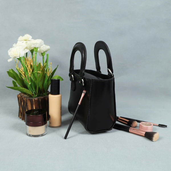 Black handbag with makeup items and a plant on a gray background