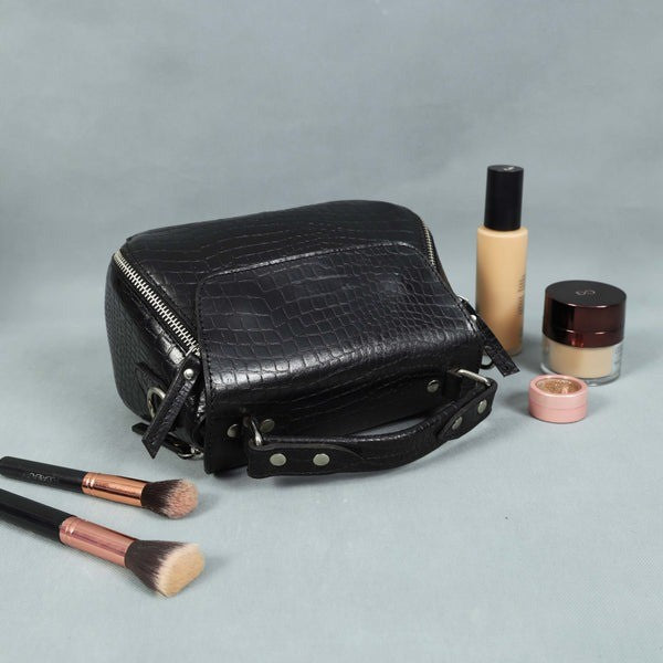 Black crocodile-patterned makeup bag with cosmetic items on a gray background