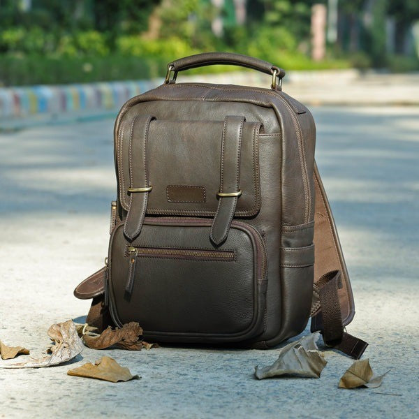 Brown leather backpack on a concrete surface with blurred greenery in the background