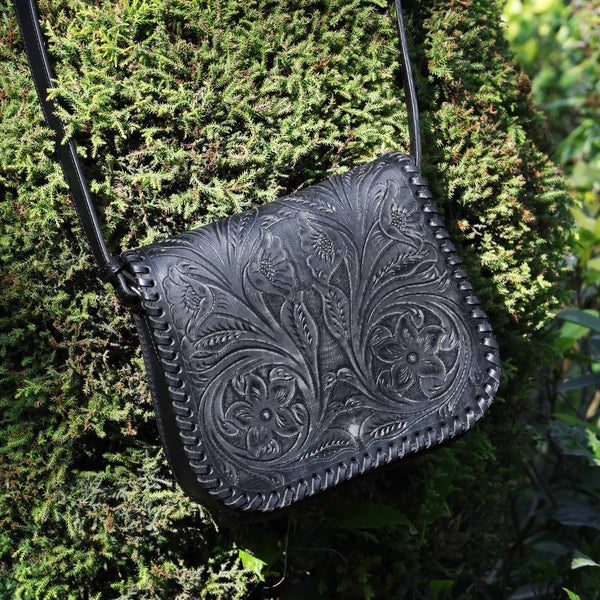 Black leather handbag with floral embossing on a green leafy background