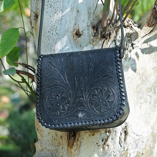 Black leather handbag with floral patterns hanging on a tree trunk