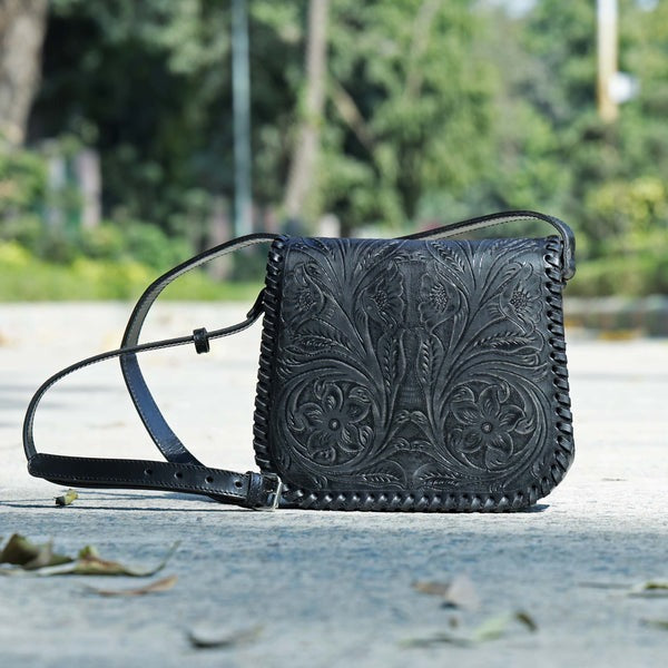 Black leather handbag with intricate patterns on a blurred natural background