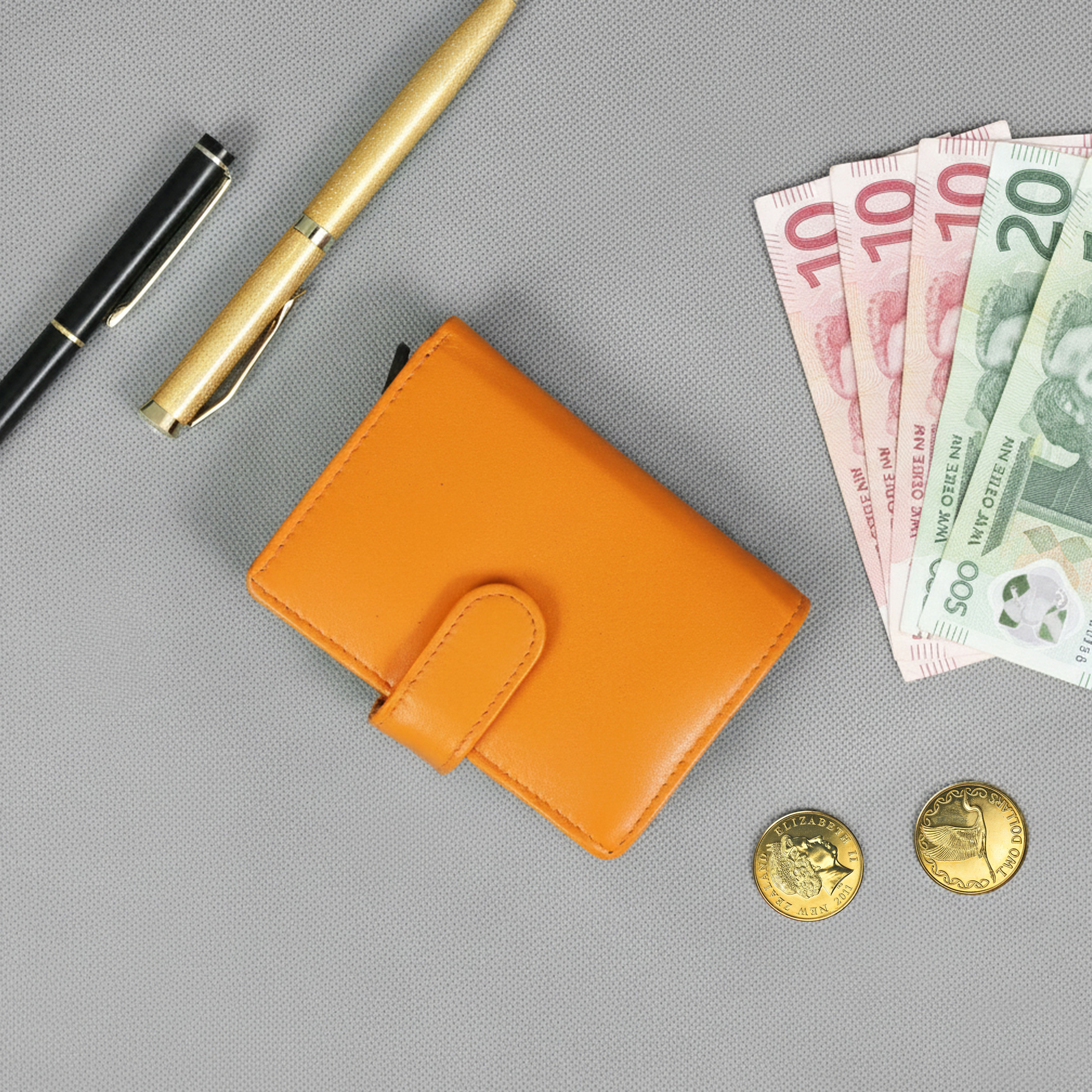 Orange wallet with money, coins, and pens on a gray background