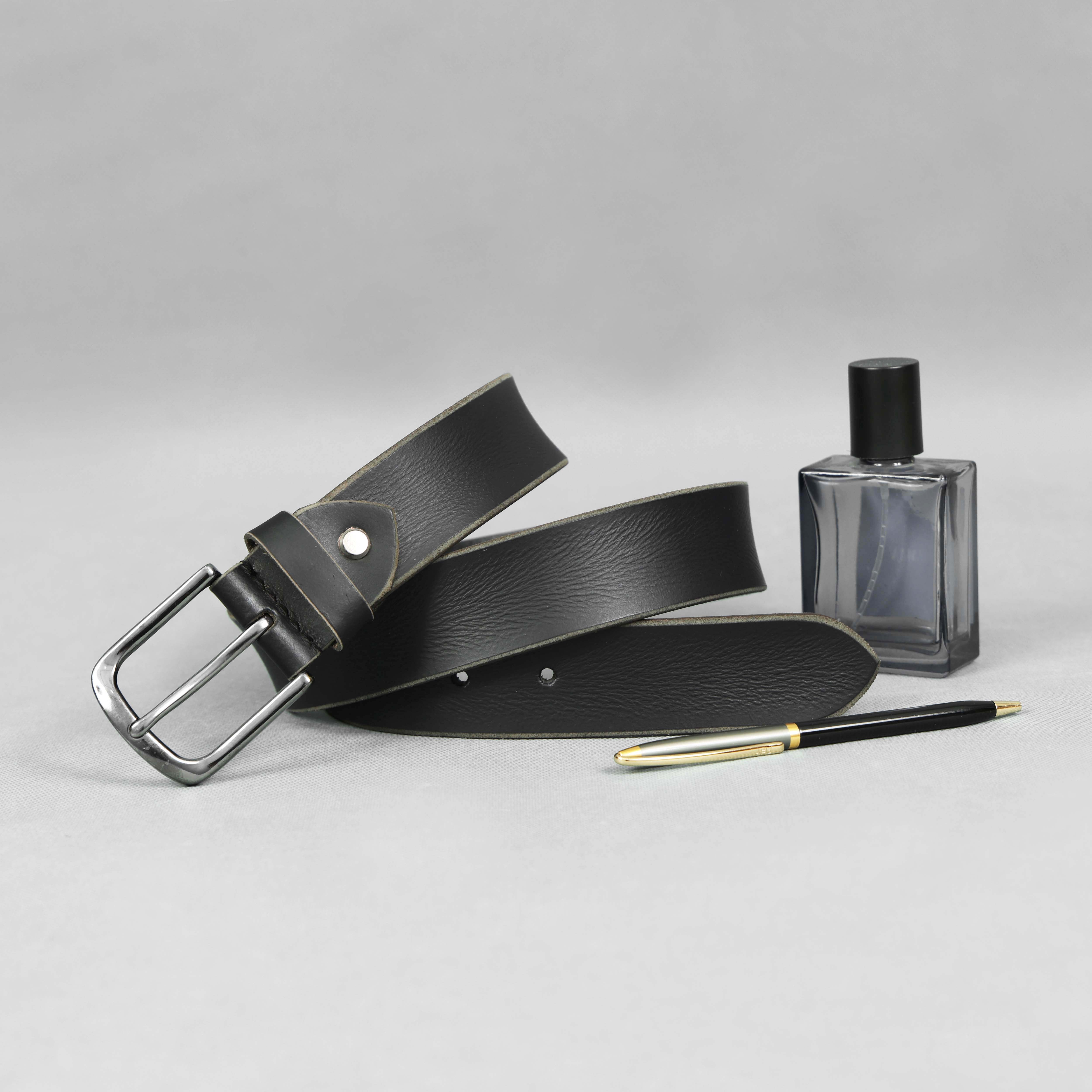 Black leather belt with silver buckle, pen, and small bottle on a light gray background