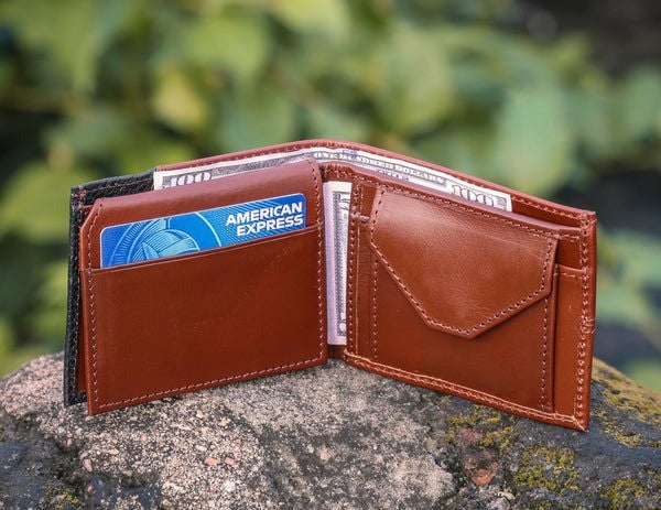 Brown leather wallet with American Express card on a stone surface with a blurred green background