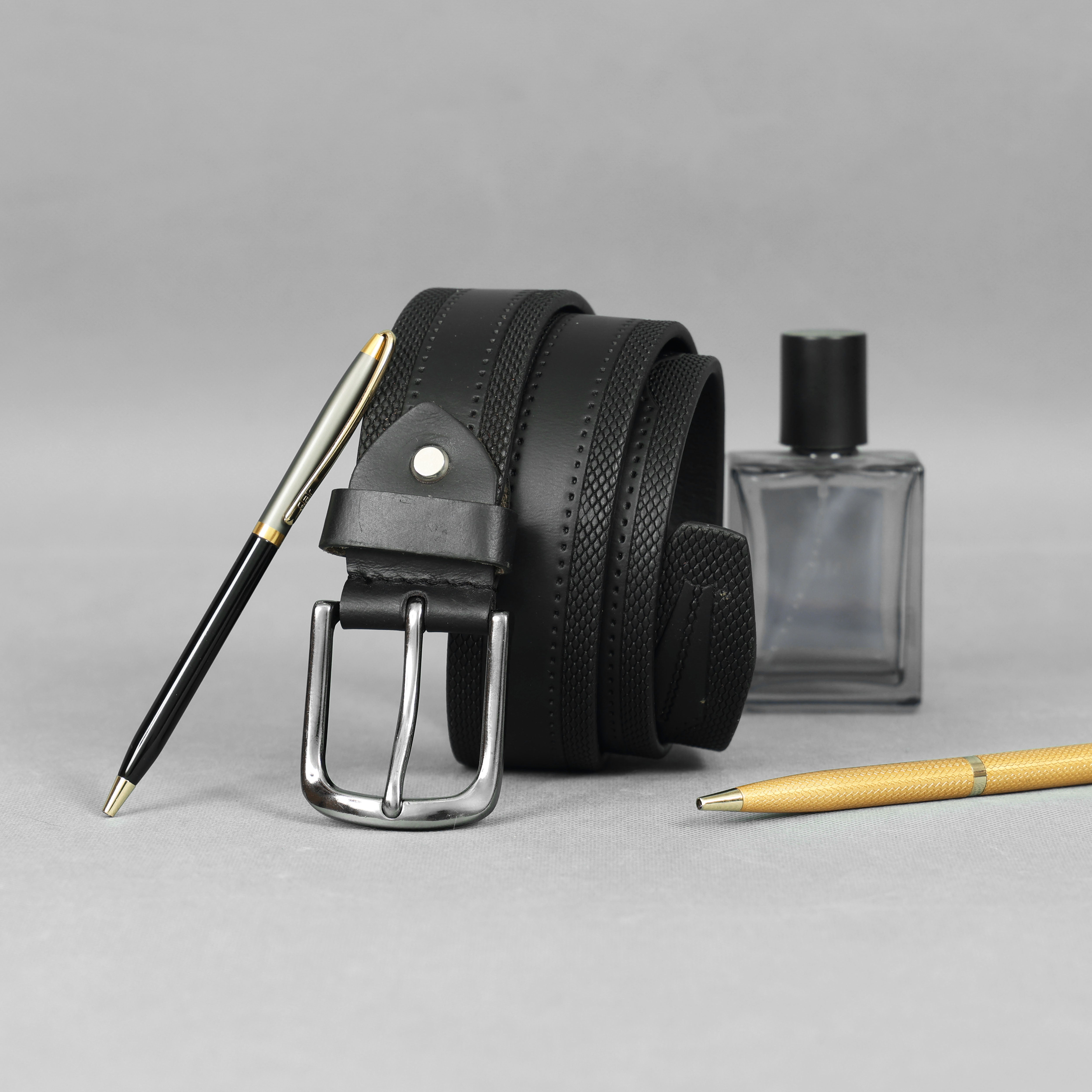 Front view of a premium black full-grain leather belt with silver buckle, elegant texture detailing, and luxury accessories including pens and cologne, designed for executive men’s fashion worldwide.