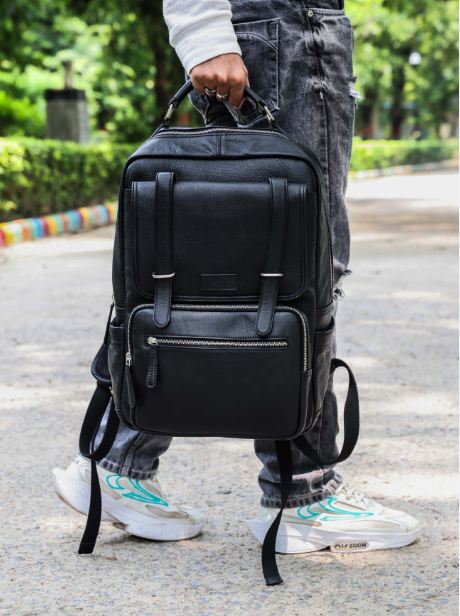 A person wearing a black leather backpack with a stylish design, featuring multiple compartments and a rich black color.