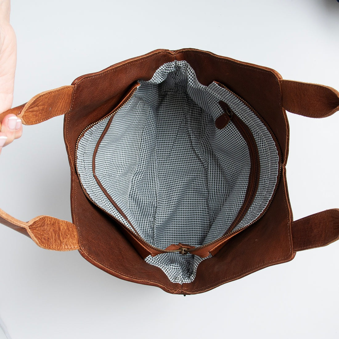 Brown leather bag with a checkered interior on a light gray background