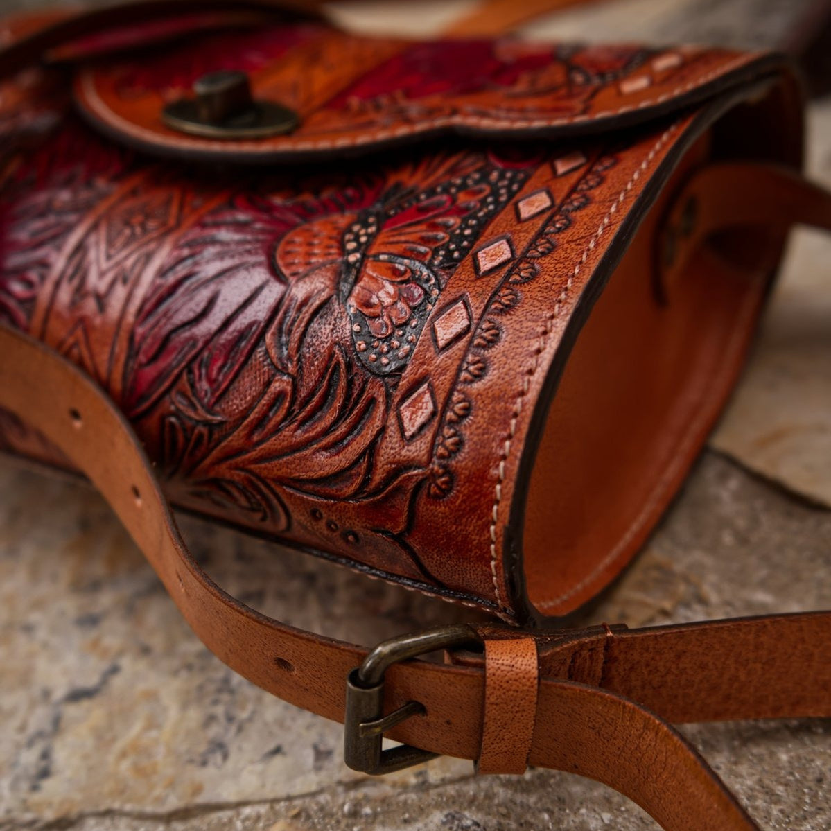 A brown leather shoulder bag by Trukado, hand-tooled with a vibrant floral and butterfly design, featuring a Western style and a twist closure