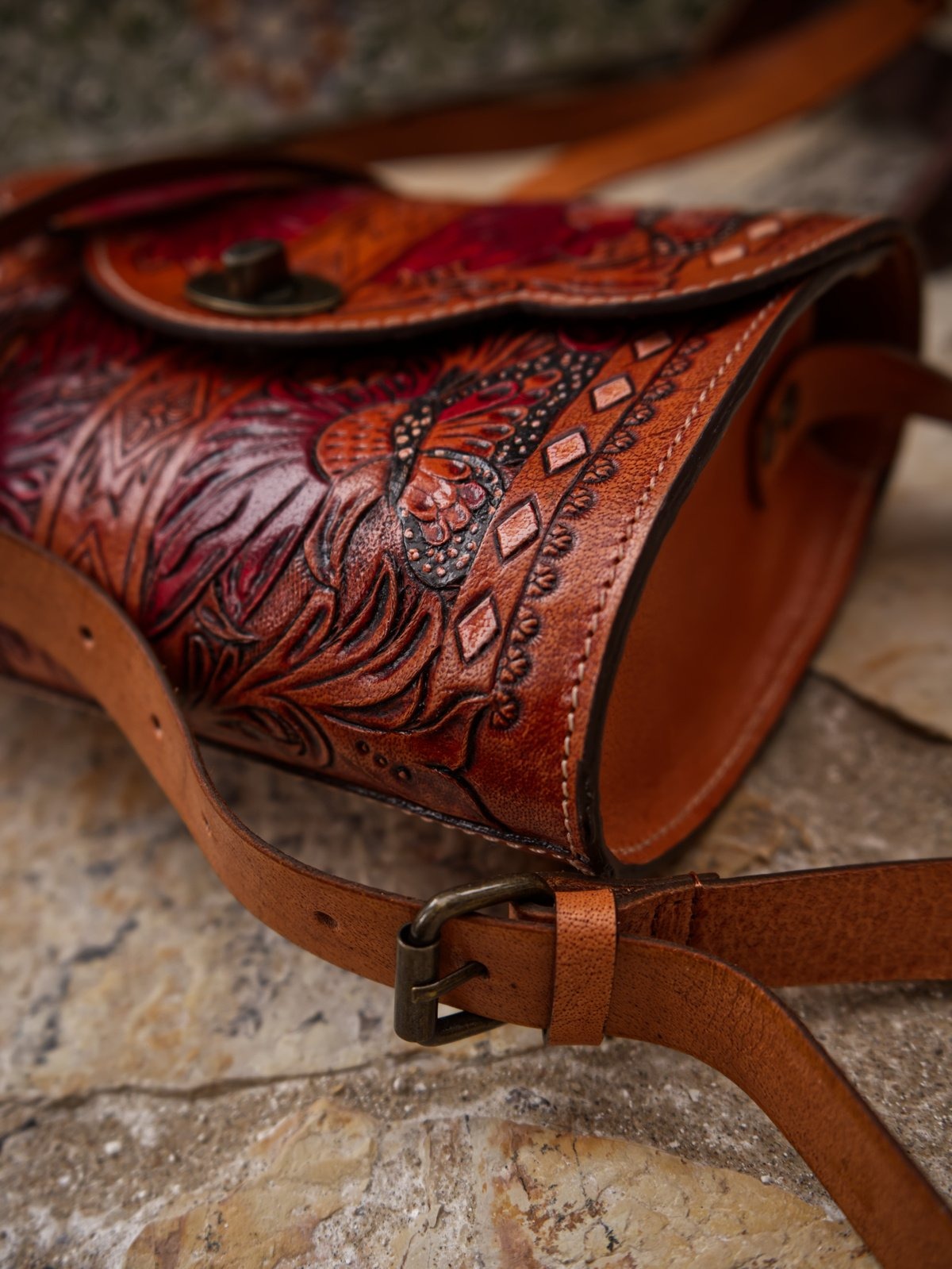 A brown leather shoulder bag by Trukado, hand-tooled with a vibrant floral and butterfly design, featuring a Western style and a twist closure