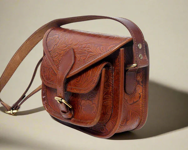 A brown leather sling bag with a floral embossed pattern, featuring a shoulder strap and a front flap with a metal buckle.