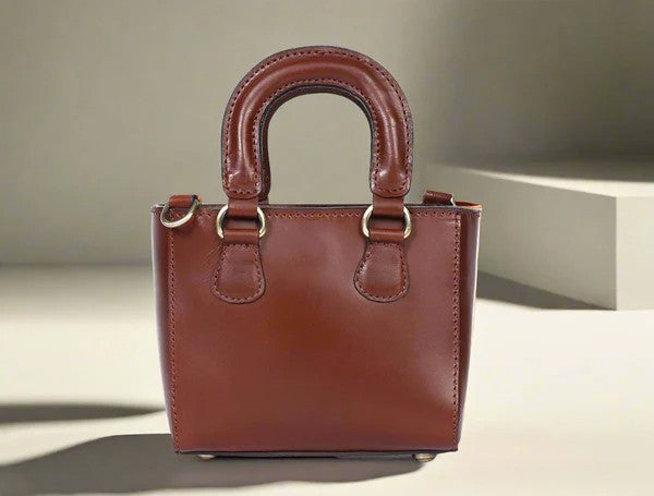 A brown leather sling bag with two handles and a detachable strap, displayed against a neutral background.
