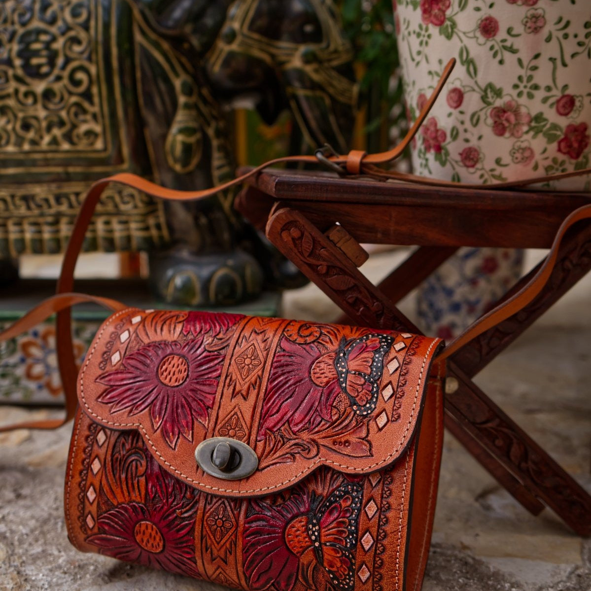 A hand-carved leather bag with a floral pattern, displayed on a wooden table.