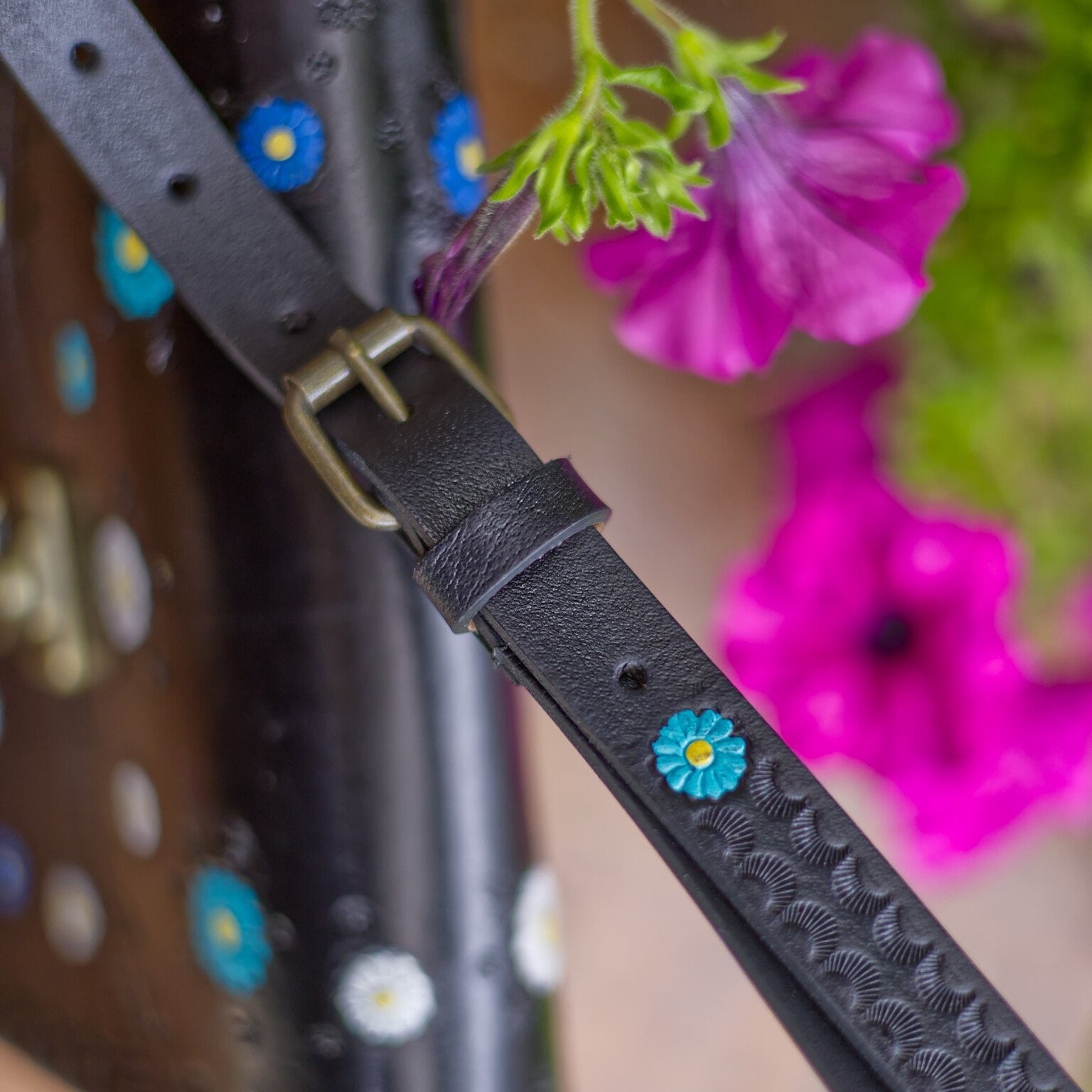 Black leather strap with floral embellishments on a blurred background of flowers and tools.