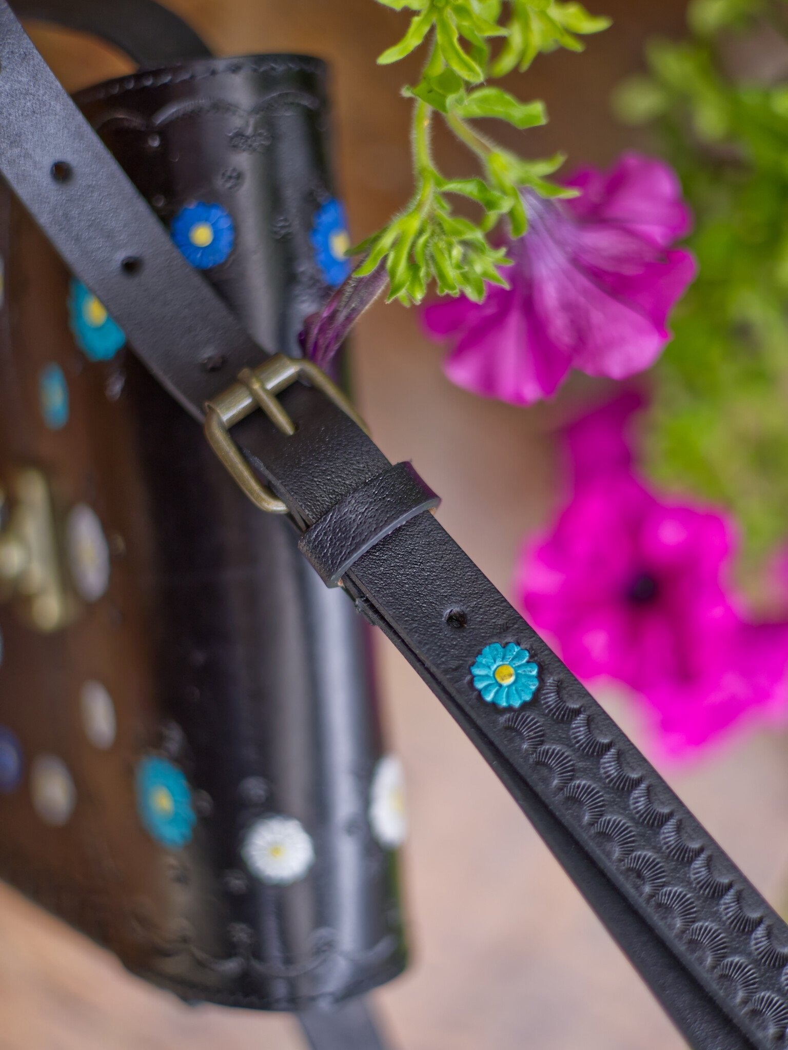 Black leather strap with floral embellishments on a blurred background of flowers and tools.