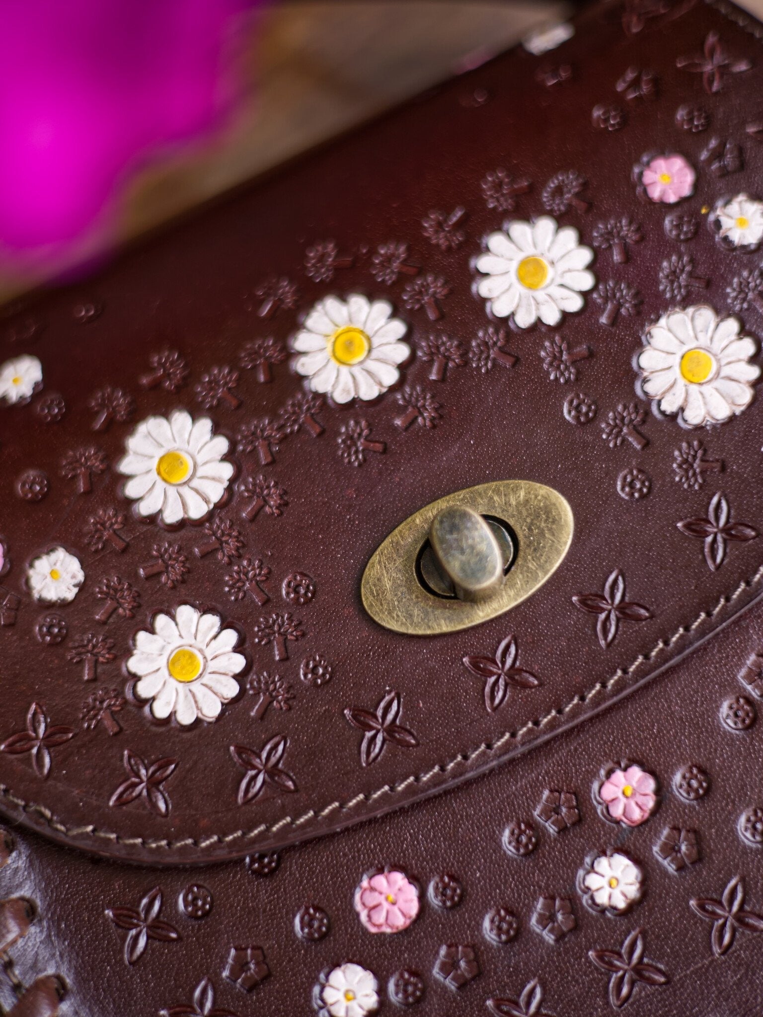 Brown leather bag with floral patterns and a decorative button.
