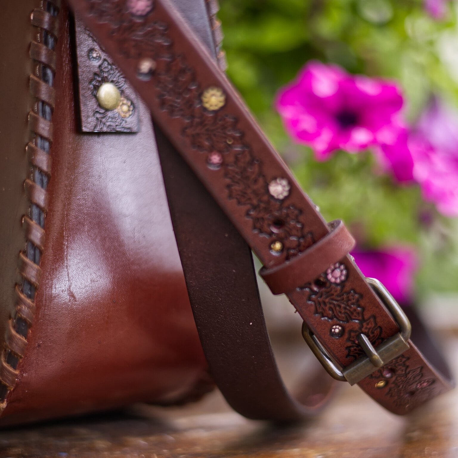 Close-up of a brown leather bag with decorative strap and floral background
