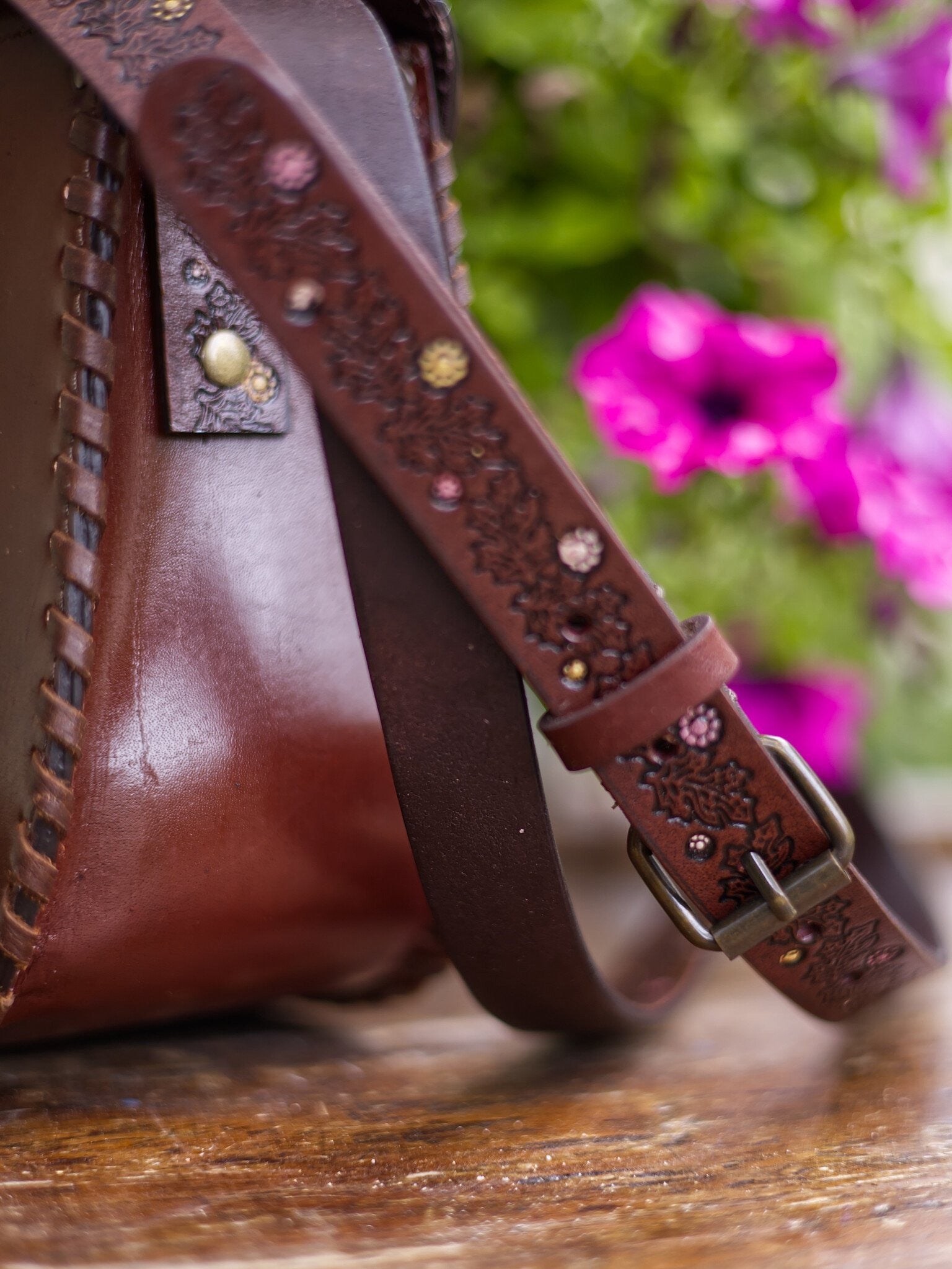 Close-up of a brown leather bag with decorative strap and floral background