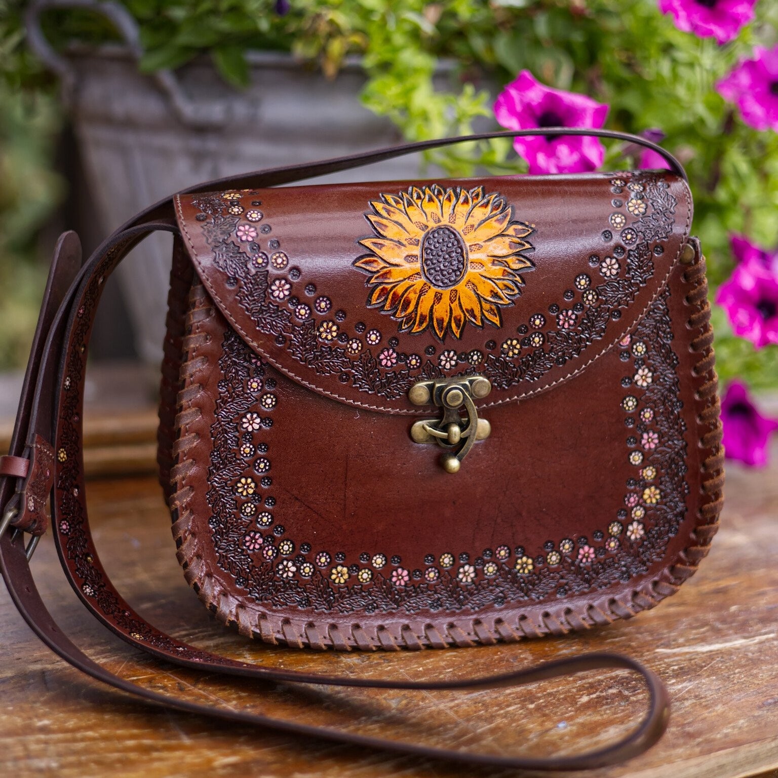 Brown leather handbag with sunflower design on a wooden surface with flowers in the background