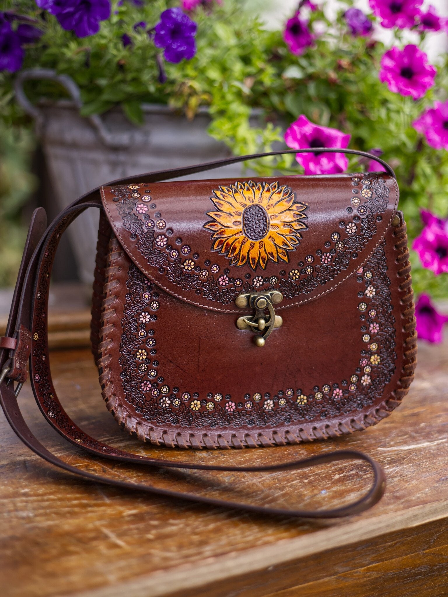 Brown leather handbag with sunflower design on a wooden surface with flowers in the background