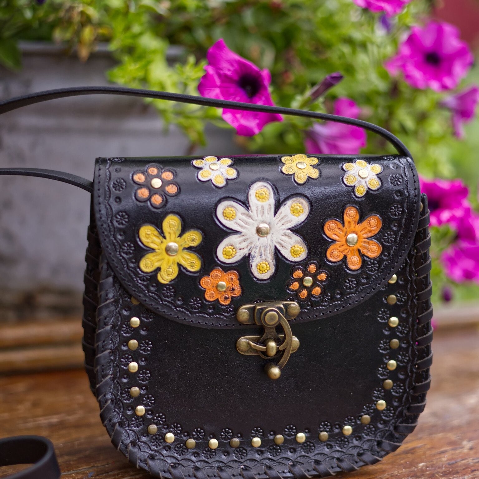 Black handbag with floral designs on a wooden surface with flowers in the background