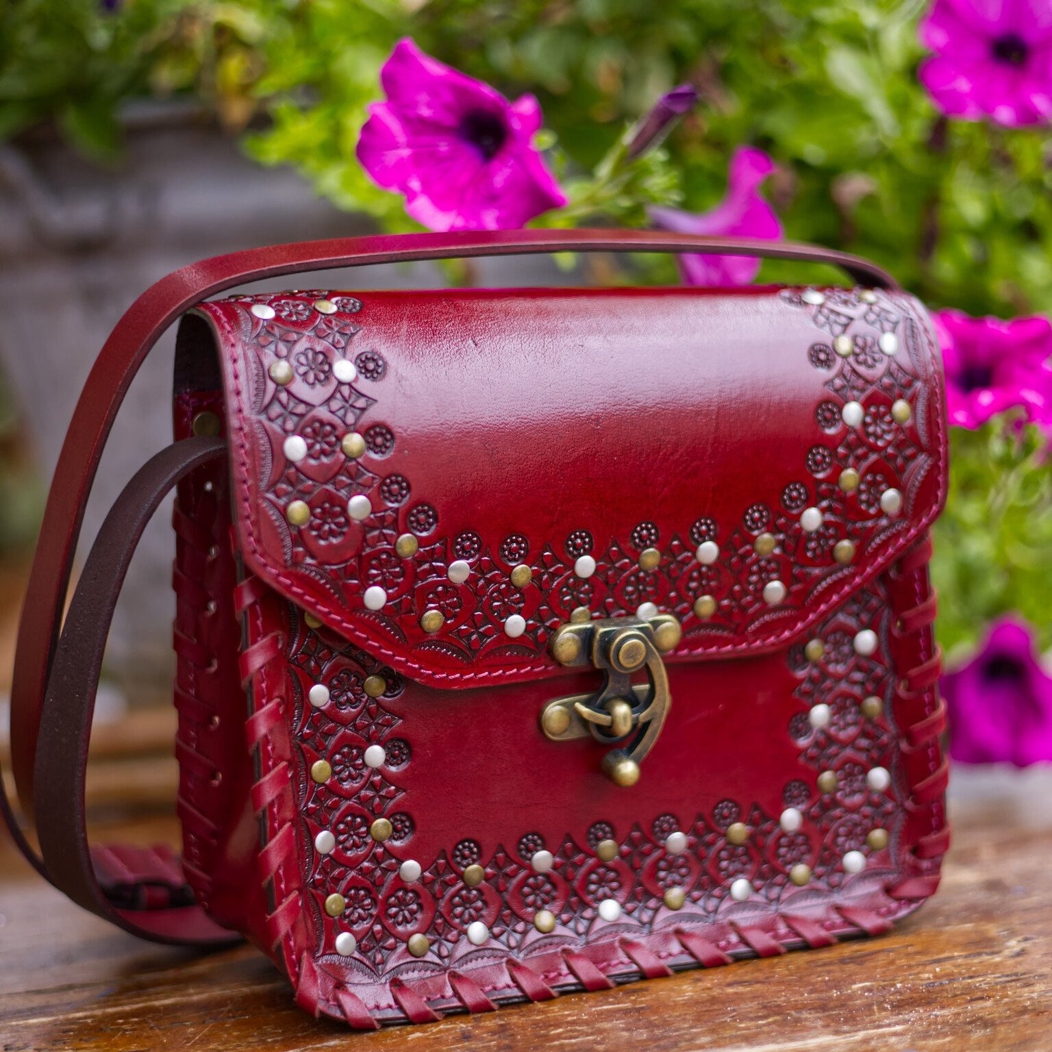 Red handbag with decorative studs on a wooden surface with flowers in the background