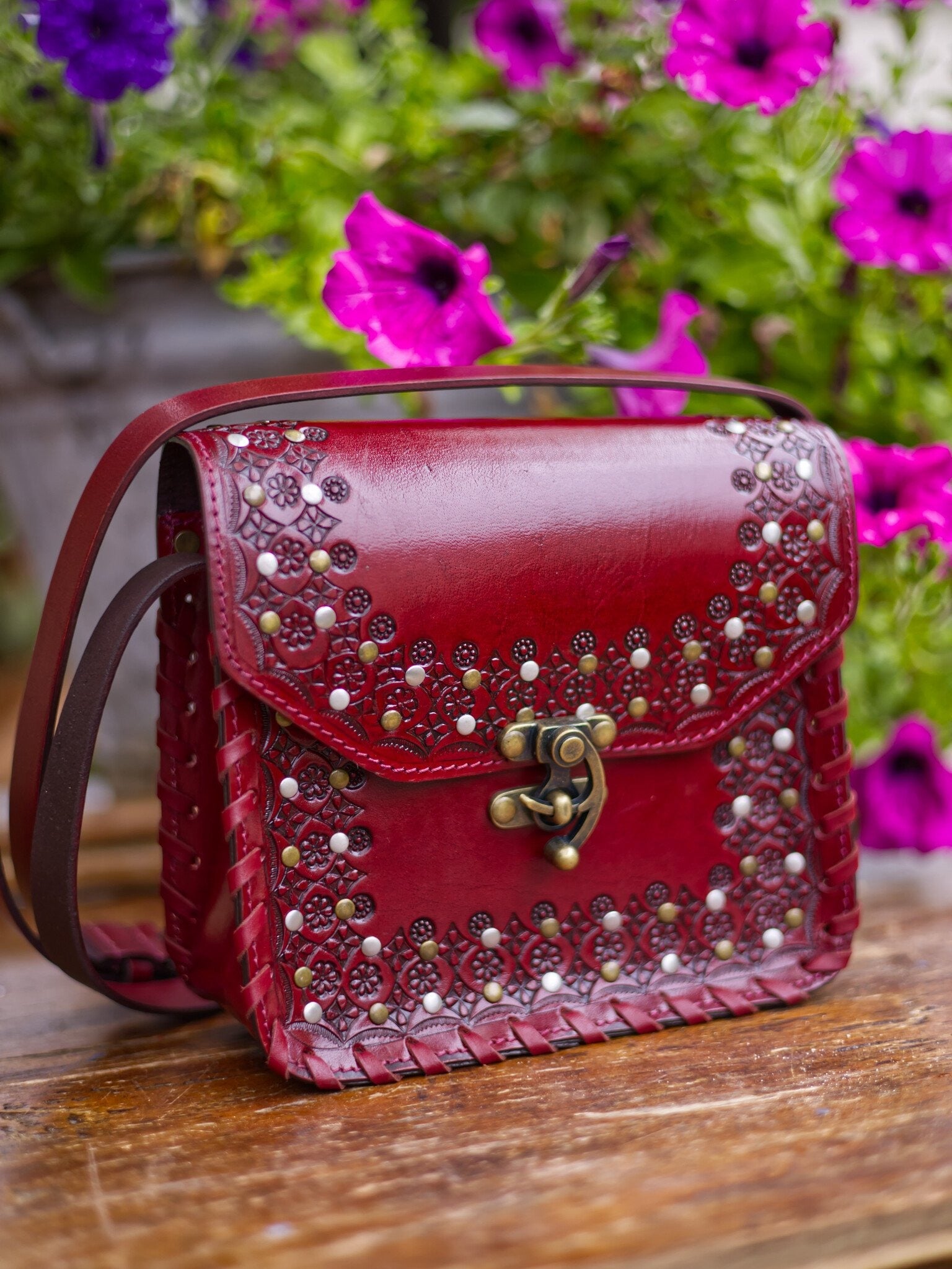 Red handbag with decorative studs on a wooden surface with flowers in the background
