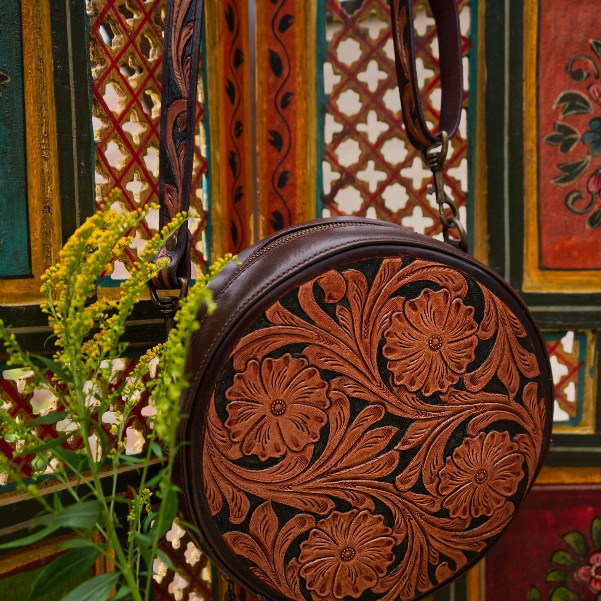 Brown leather bag with floral patterns against a colorful, patterned wall.
