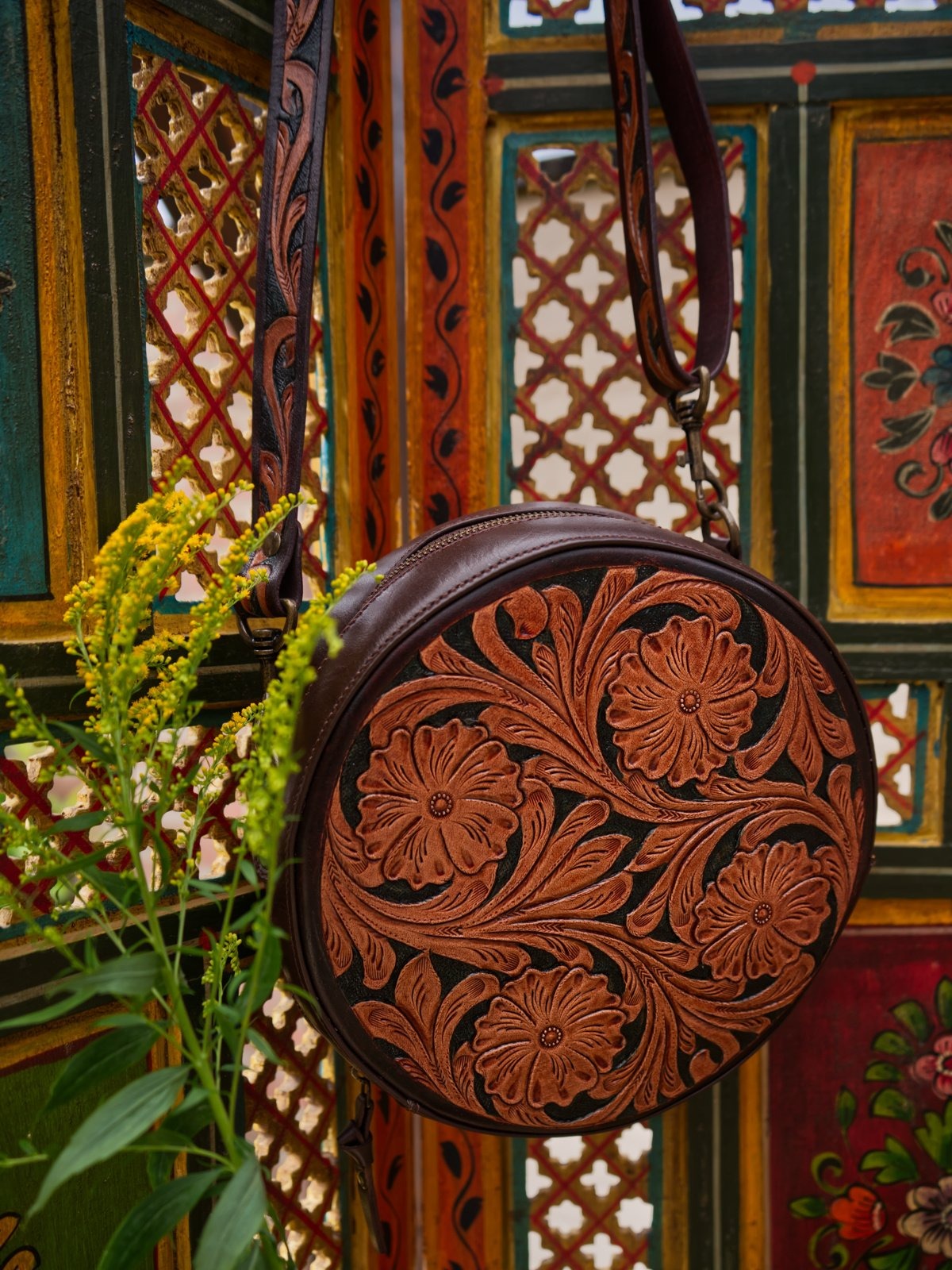 Brown leather bag with floral patterns against a colorful, patterned wall.
