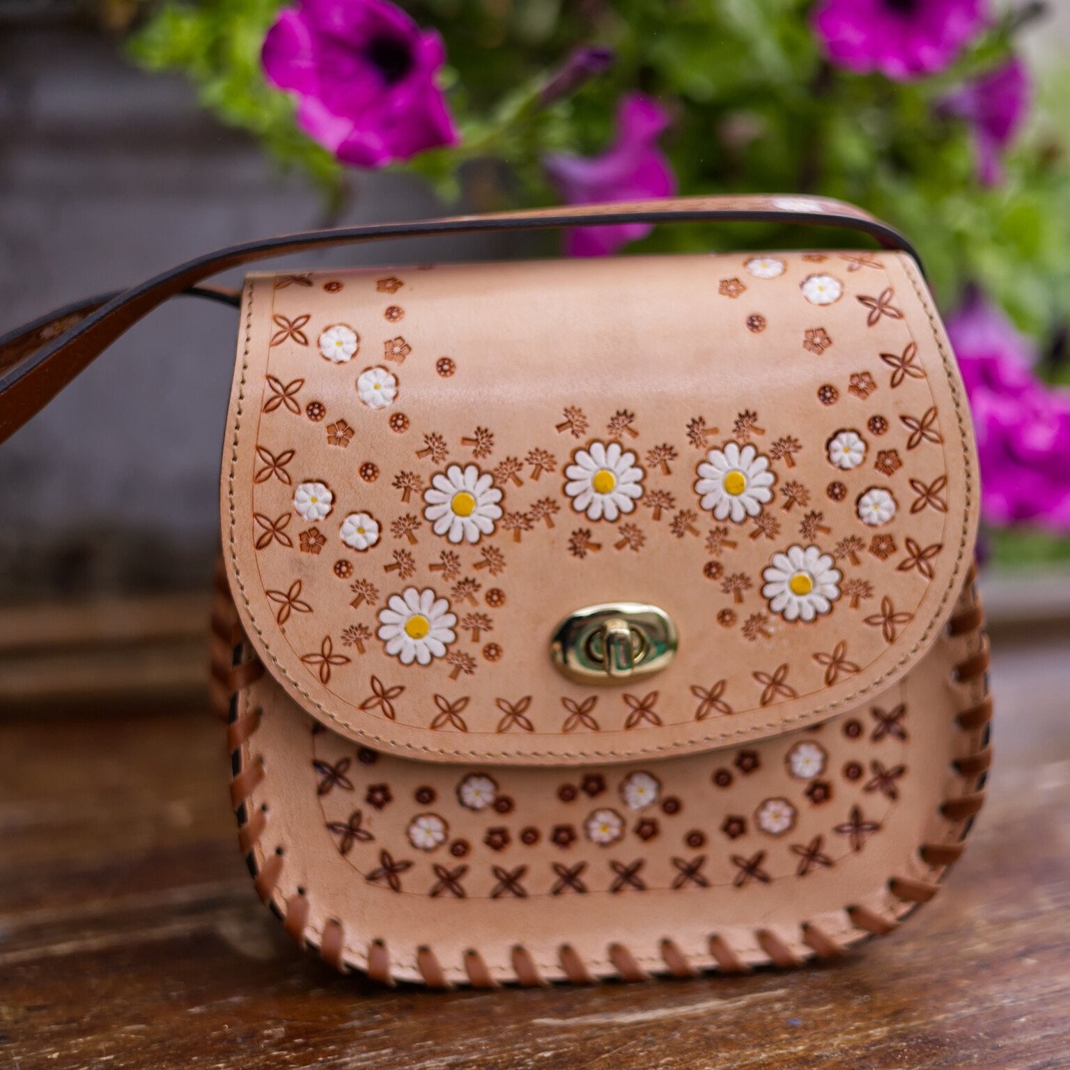 Leather handbag with floral patterns on a wooden surface with flowers in the background