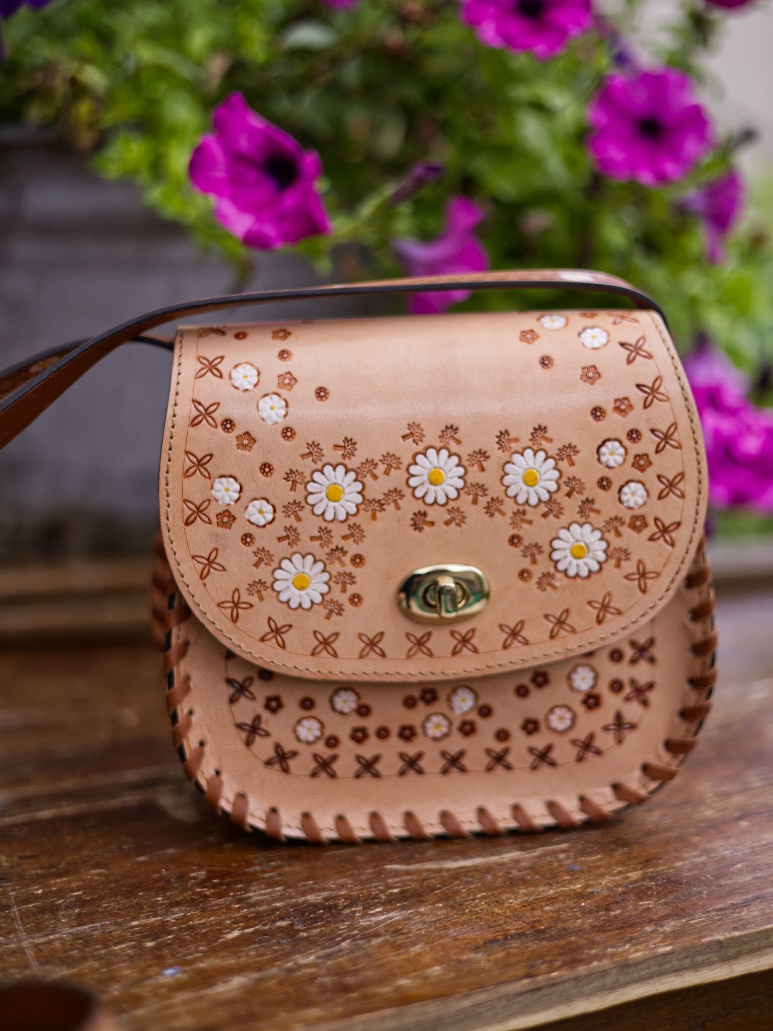 Leather handbag with floral patterns on a wooden surface with flowers in the background