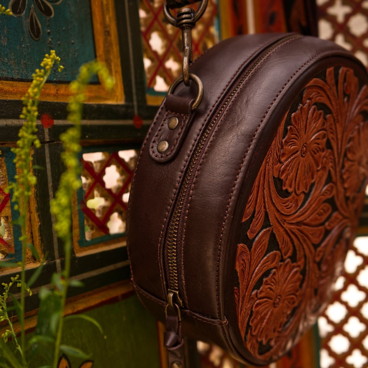 Brown leather bag with intricate designs against a decorative background