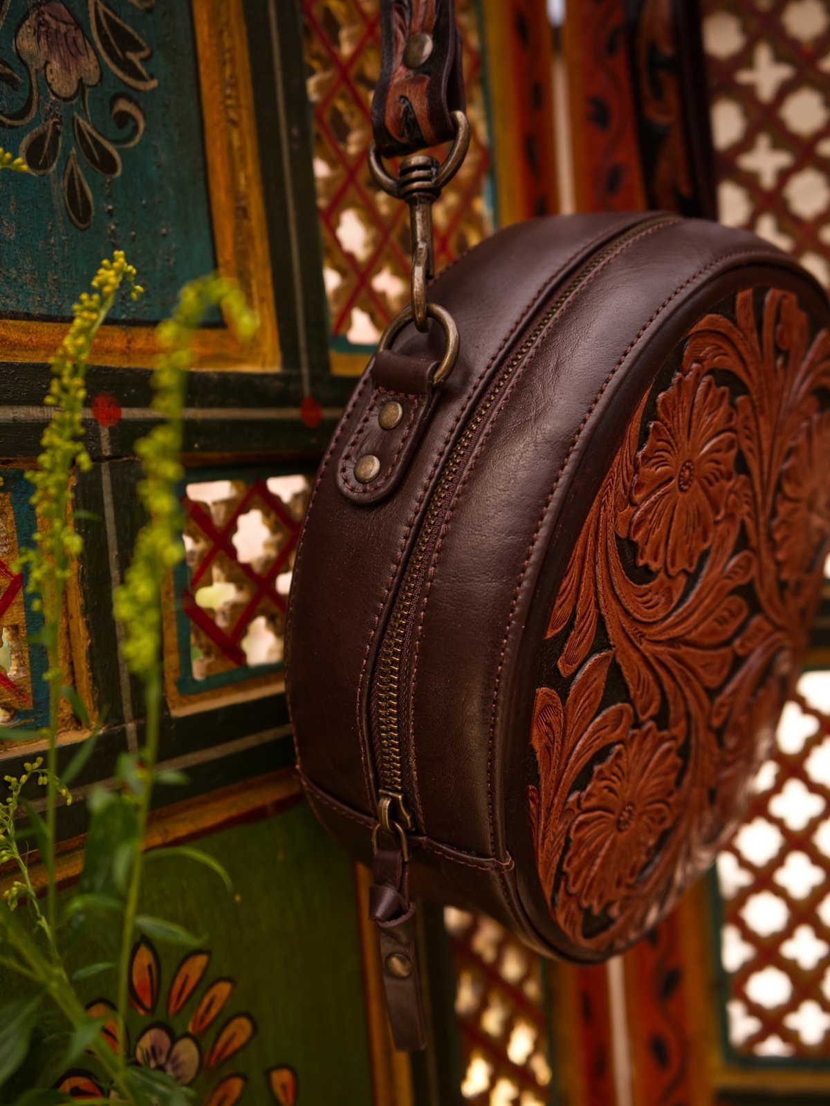 Brown leather bag with intricate designs against a decorative background