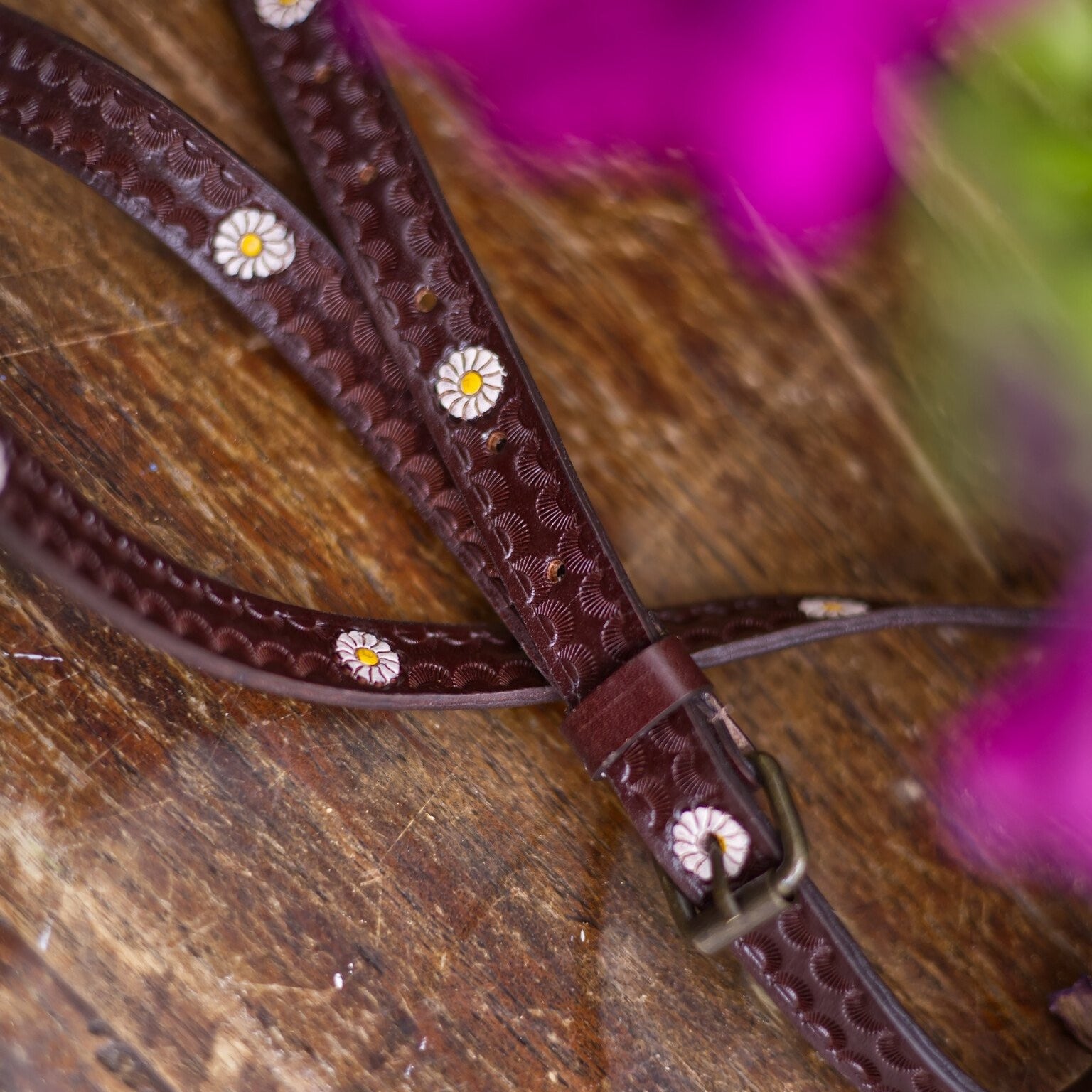 Brown leather bridle with floral patterns on a wooden surface