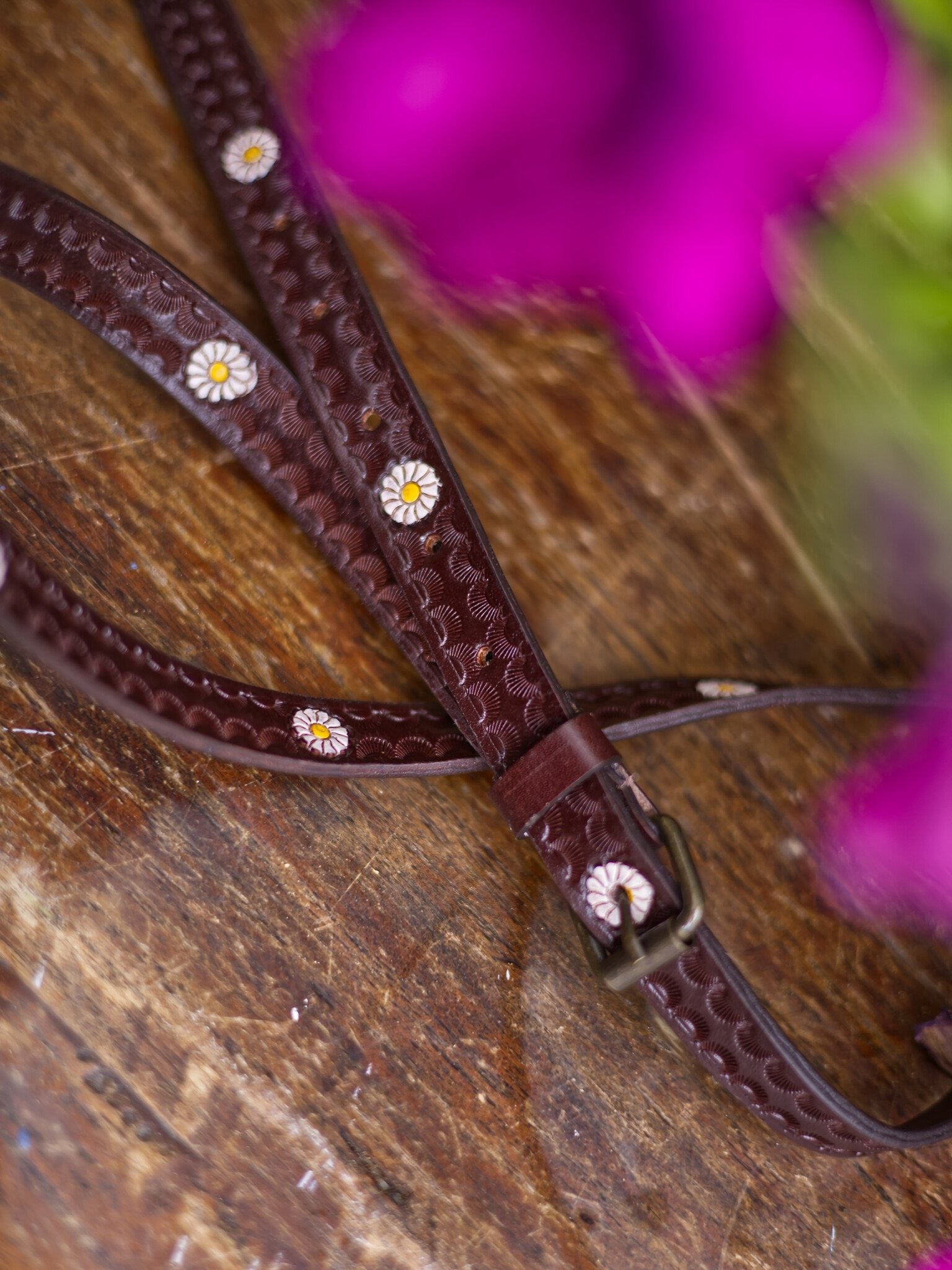 Brown leather bridle with floral patterns on a wooden surface