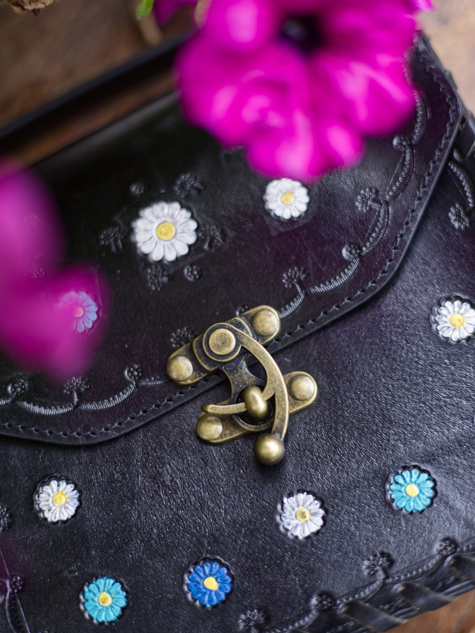 Black handbag with floral embellishments and a gold clasp, with pink flowers in the background.