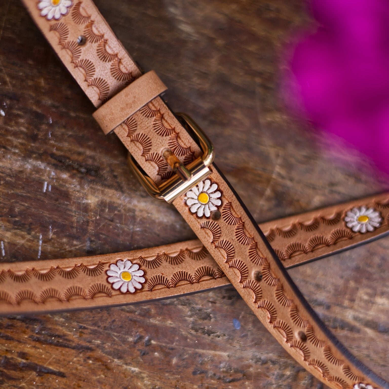 Brown leather strap with floral patterns and a gold buckle on a wooden surface.