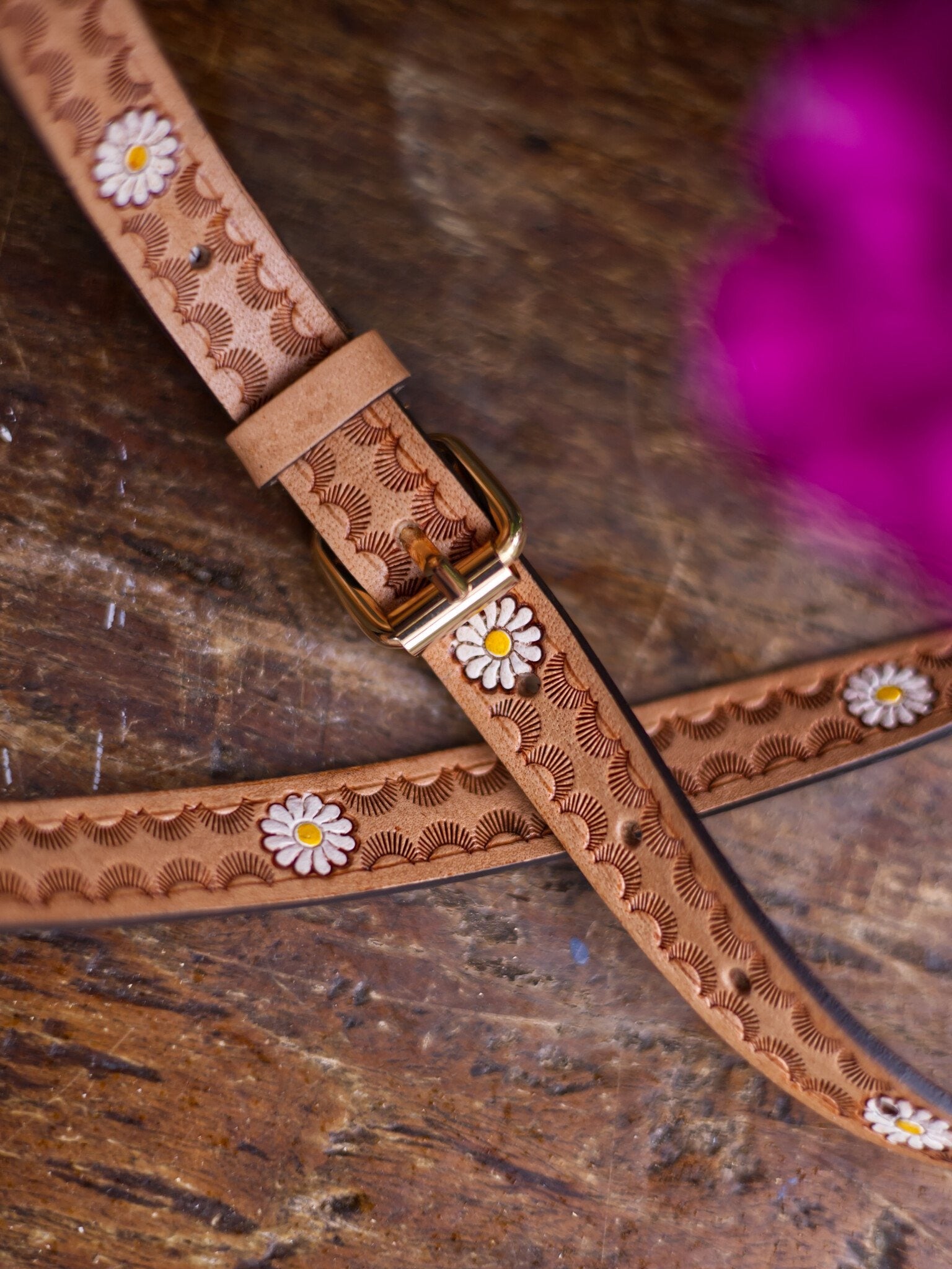 Brown leather strap with floral patterns and a gold buckle on a wooden surface.