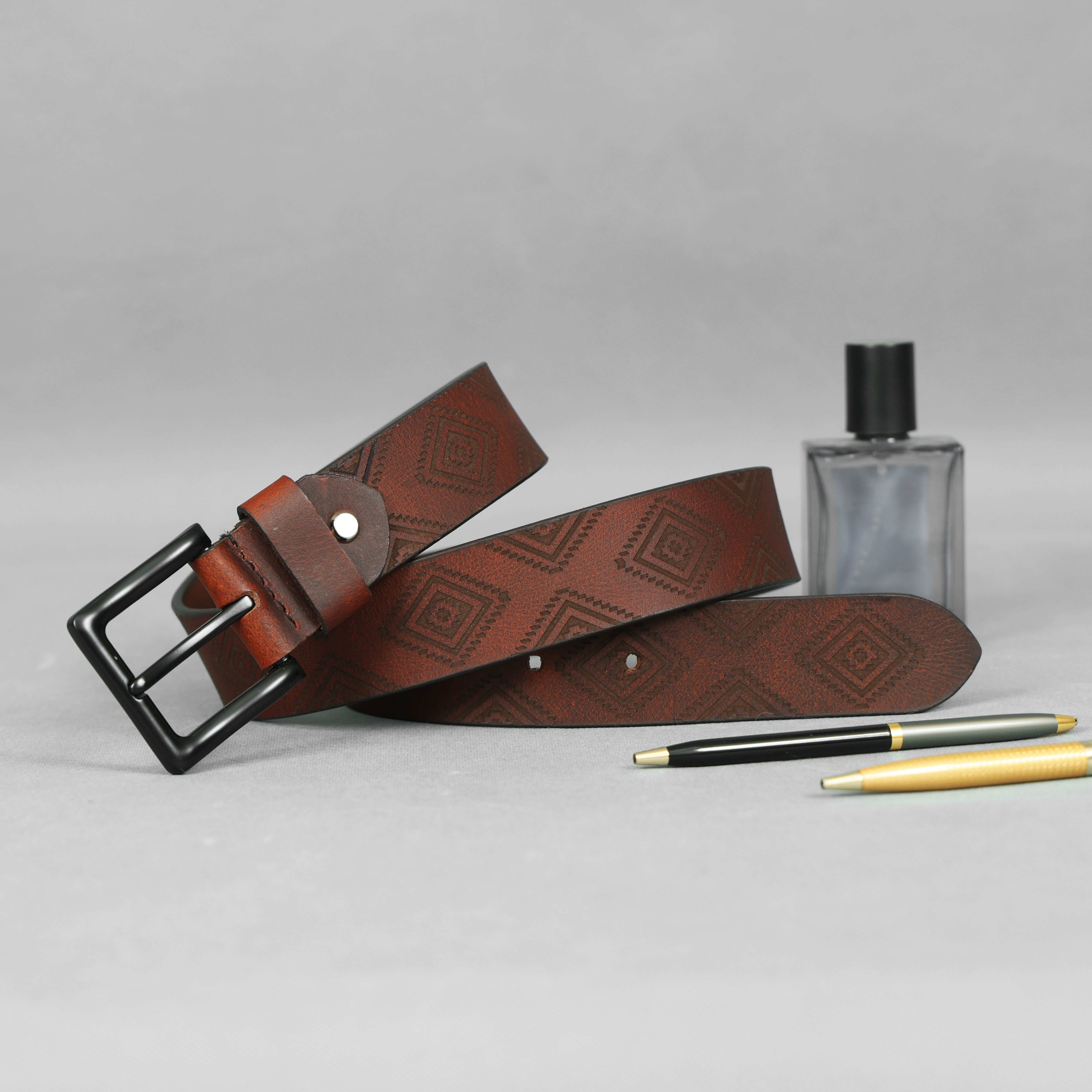 Brown leather belt with geometric pattern, black pen, and clear bottle on gray background