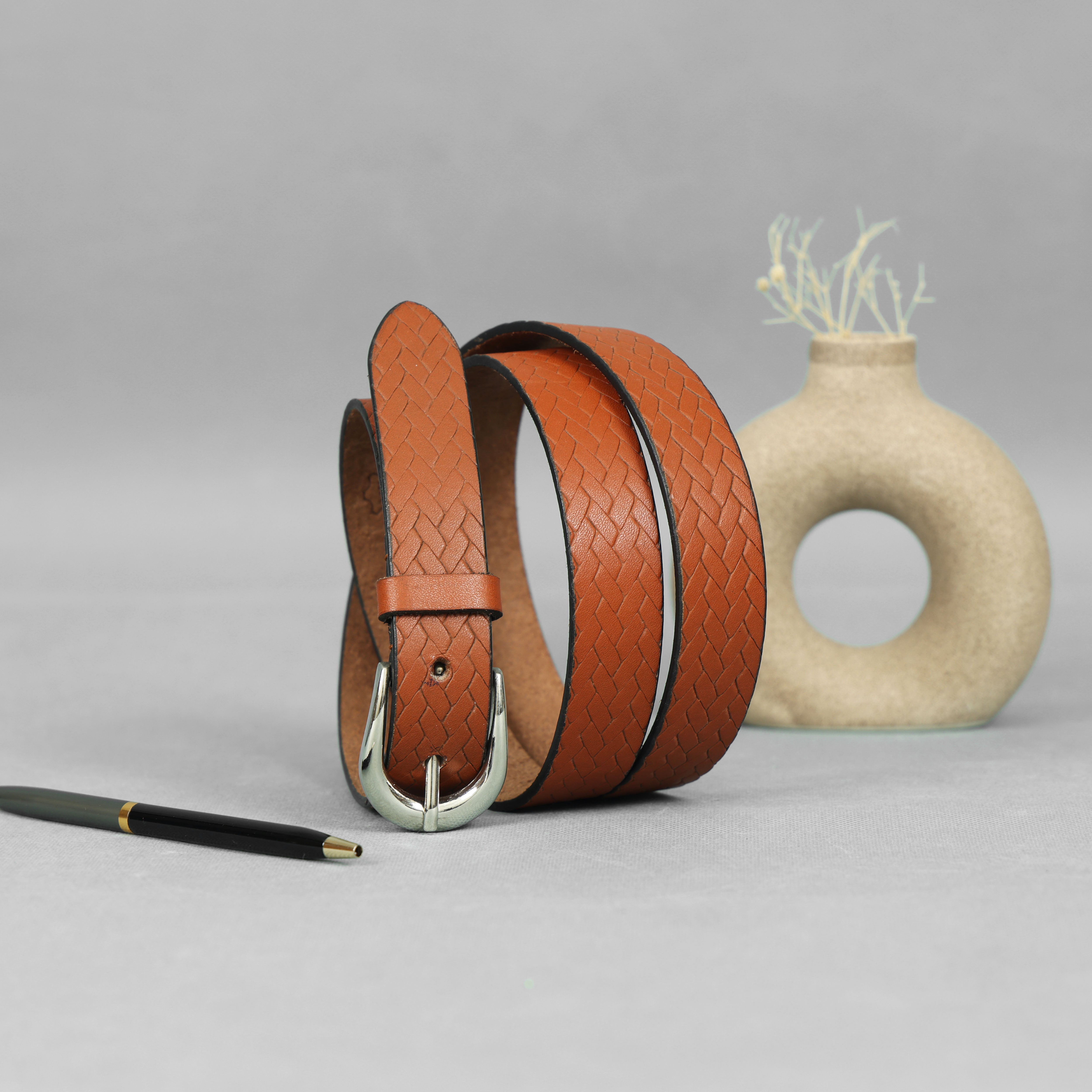 Brown leather belt with woven pattern on a gray surface with a vase in the background