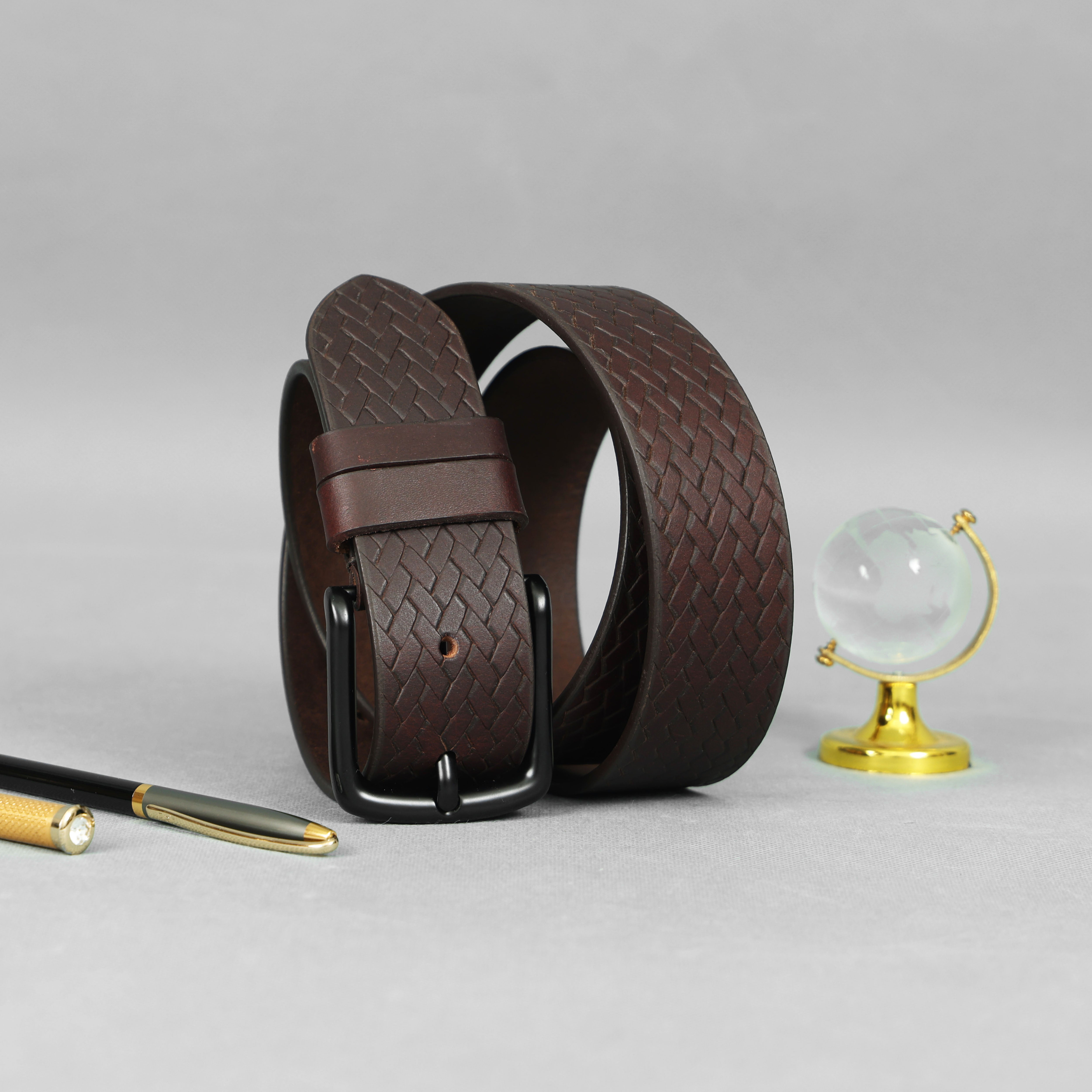 Brown leather belt on a gray surface with a pen and small globe in the background