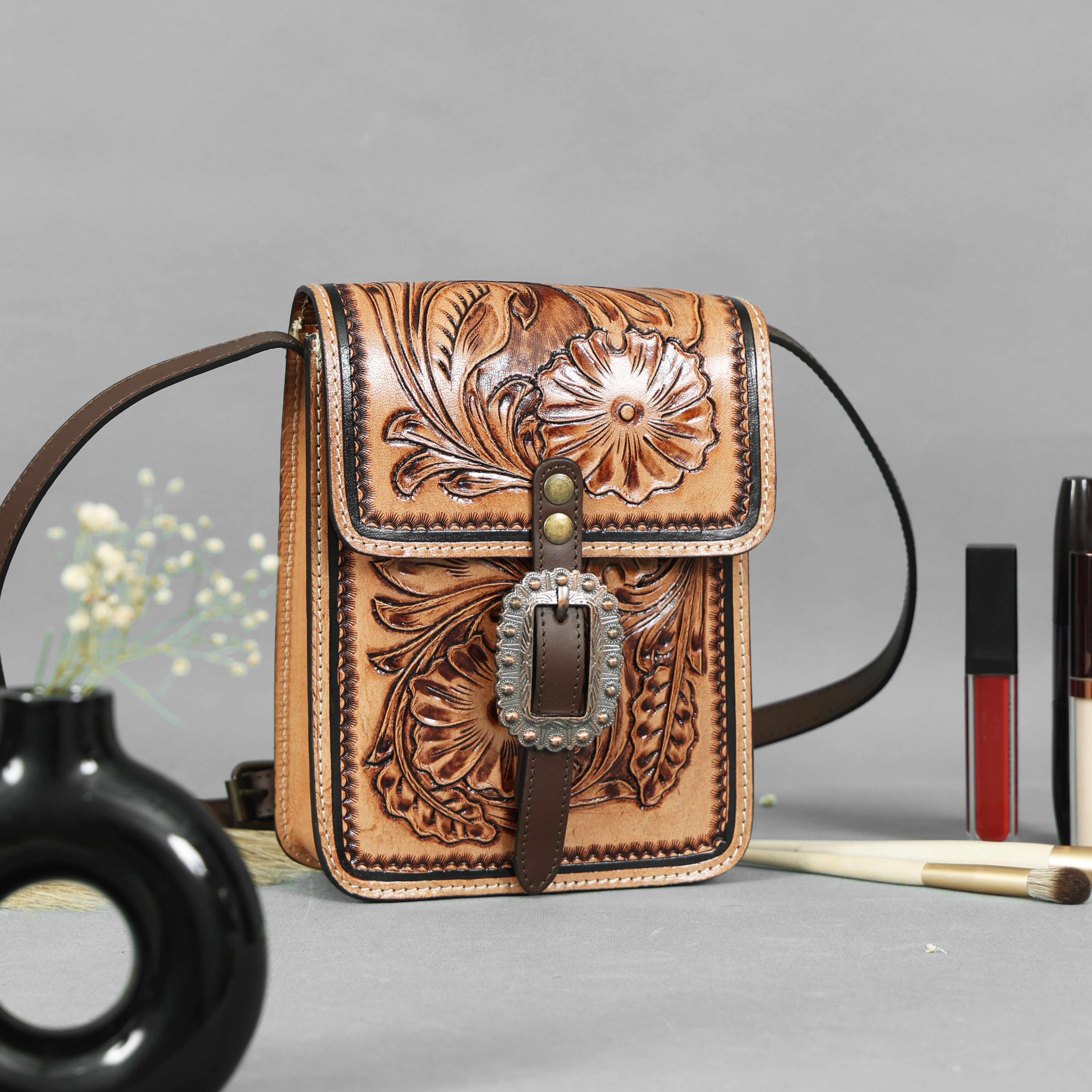 Brown leather crossbody bag with floral patterns on a gray background