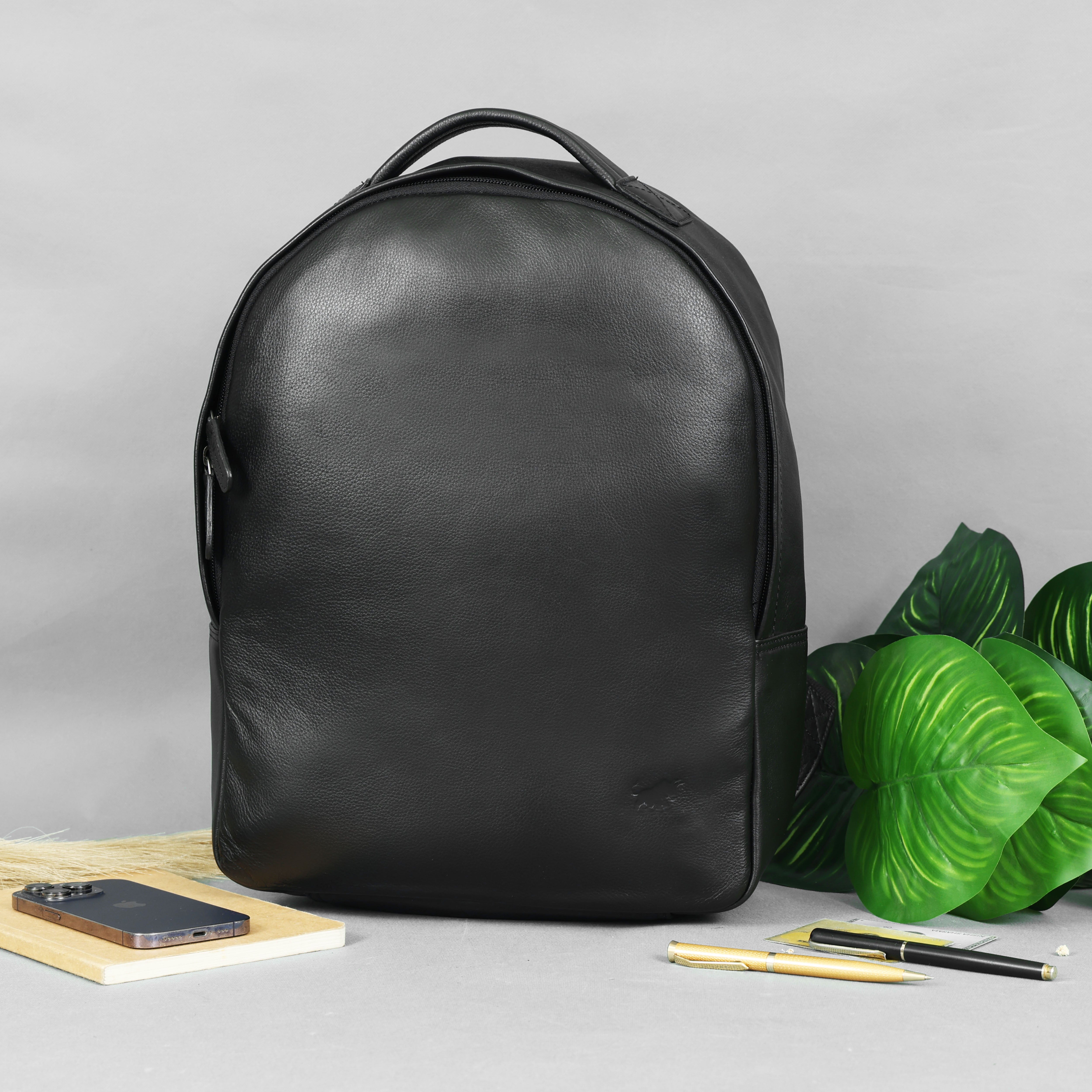GM Leather Classic Black Leather Backpack with minimalist design, rounded top, and subtle side pocket, displayed with a phone and pens. Available at GM Leather Auckland.