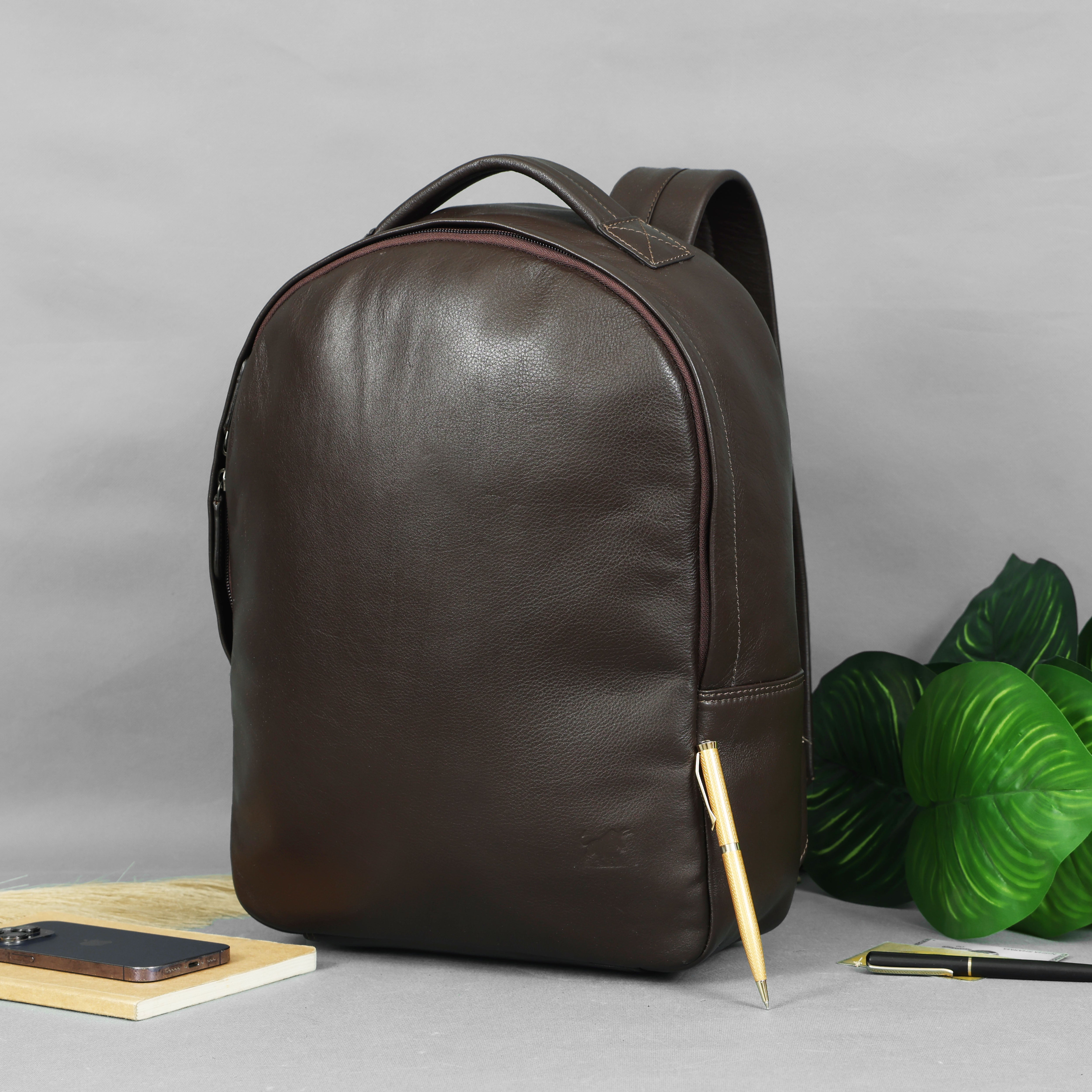 GM Leather Classic Brown Leather Backpack with minimalist design, rounded top, and subtle side pocket, displayed with a phone and pens. Available at GM Leather Auckland.