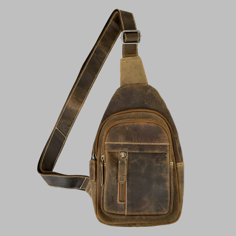 Men's brown full-grain leather sling bag with two vertical front zipper pockets and an adjustable shoulder strap