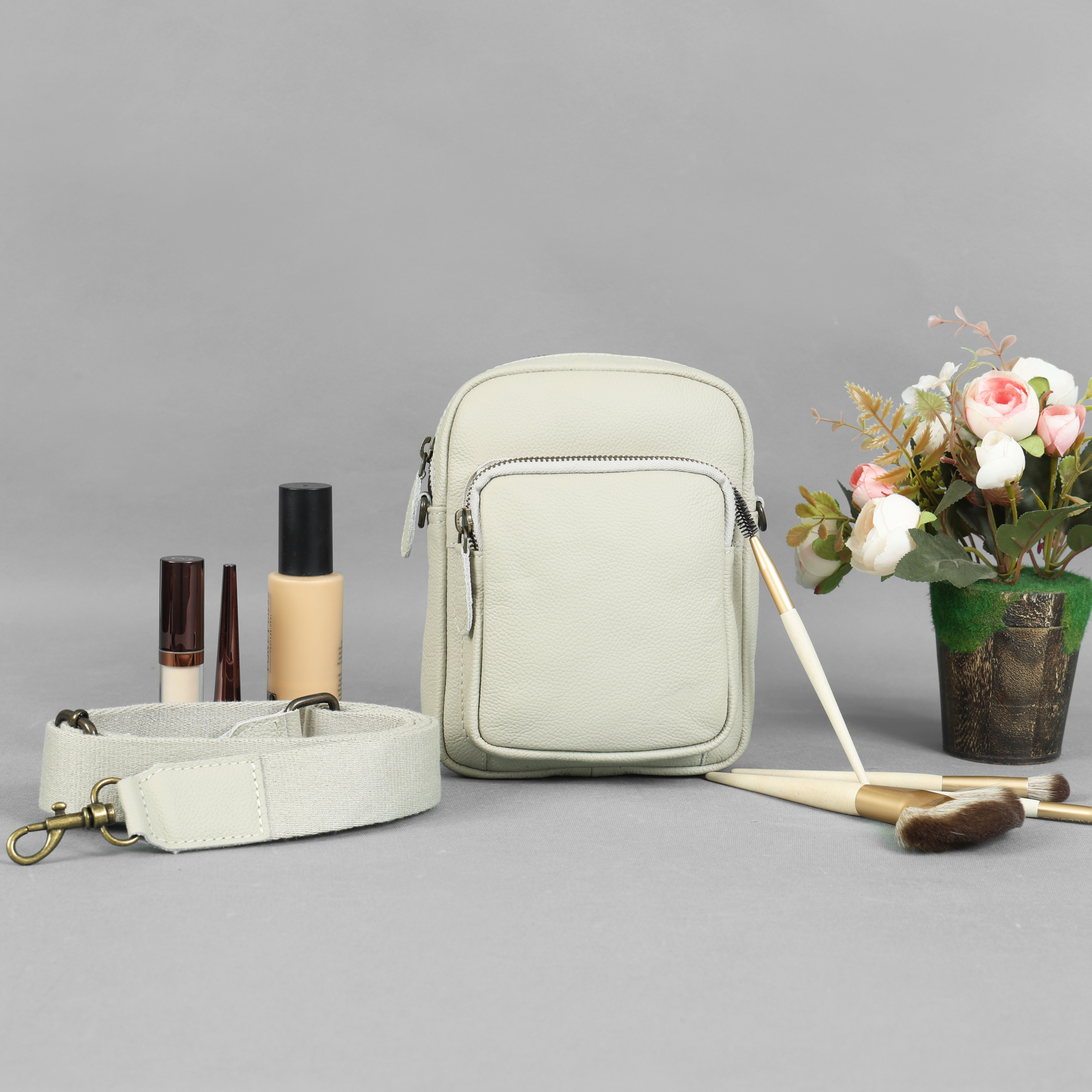 Premium beige genuine leather mini crossbody bag with brass hardware and thick canvas strap by GM Leather Auckland, styled with makeup brushes.