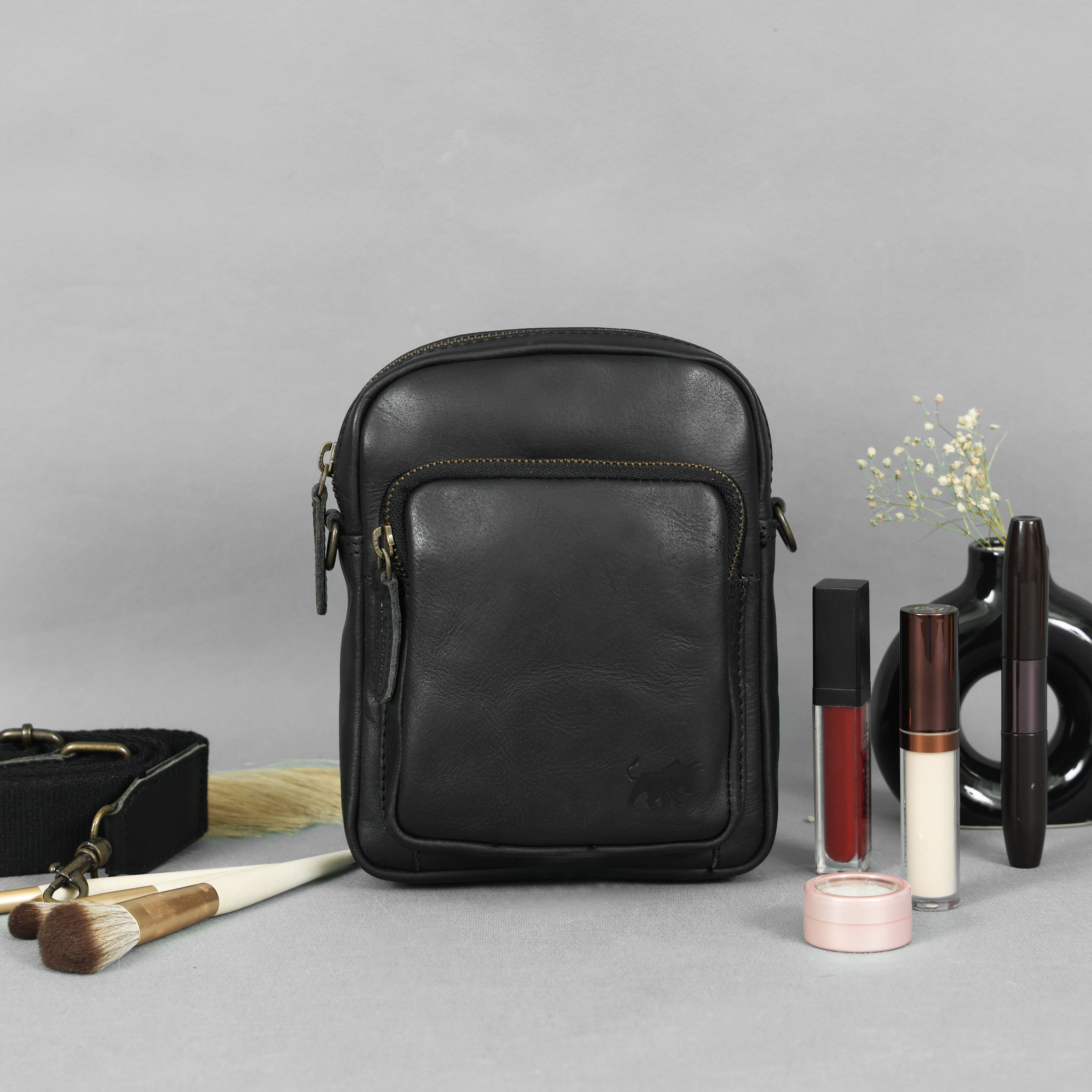 Premium black genuine leather mini crossbody bag with brass hardware and thick canvas strap by GM Leather Auckland, styled with makeup brushes.