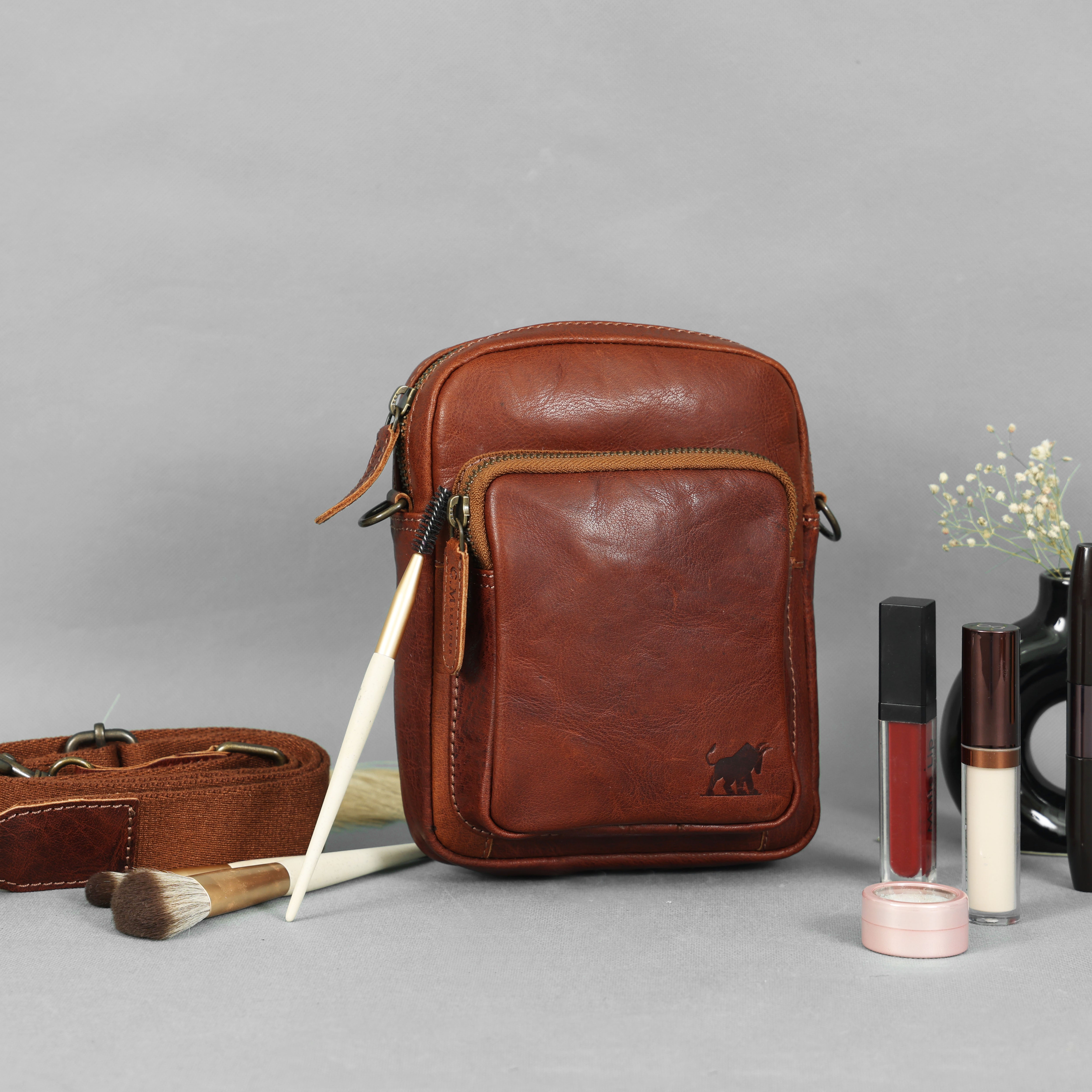 Premium brown genuine leather mini crossbody bag with brass hardware and thick canvas strap by GM Leather Auckland, styled with makeup brushes.