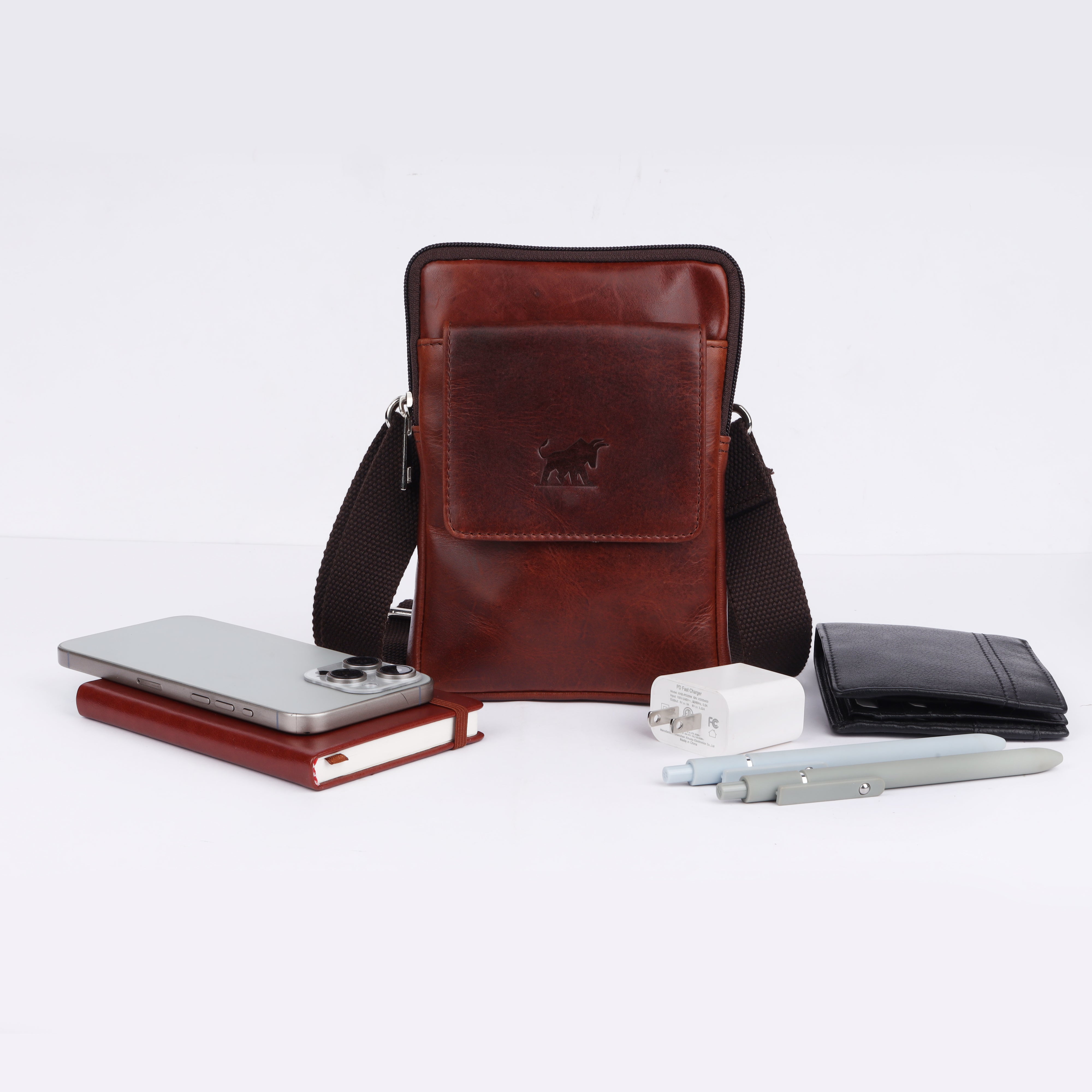 Flat-lay presentation of the GM Leather brown shoulder pouch styled with daily essentials including a smartphone, notebook, wallet, and tech accessories.